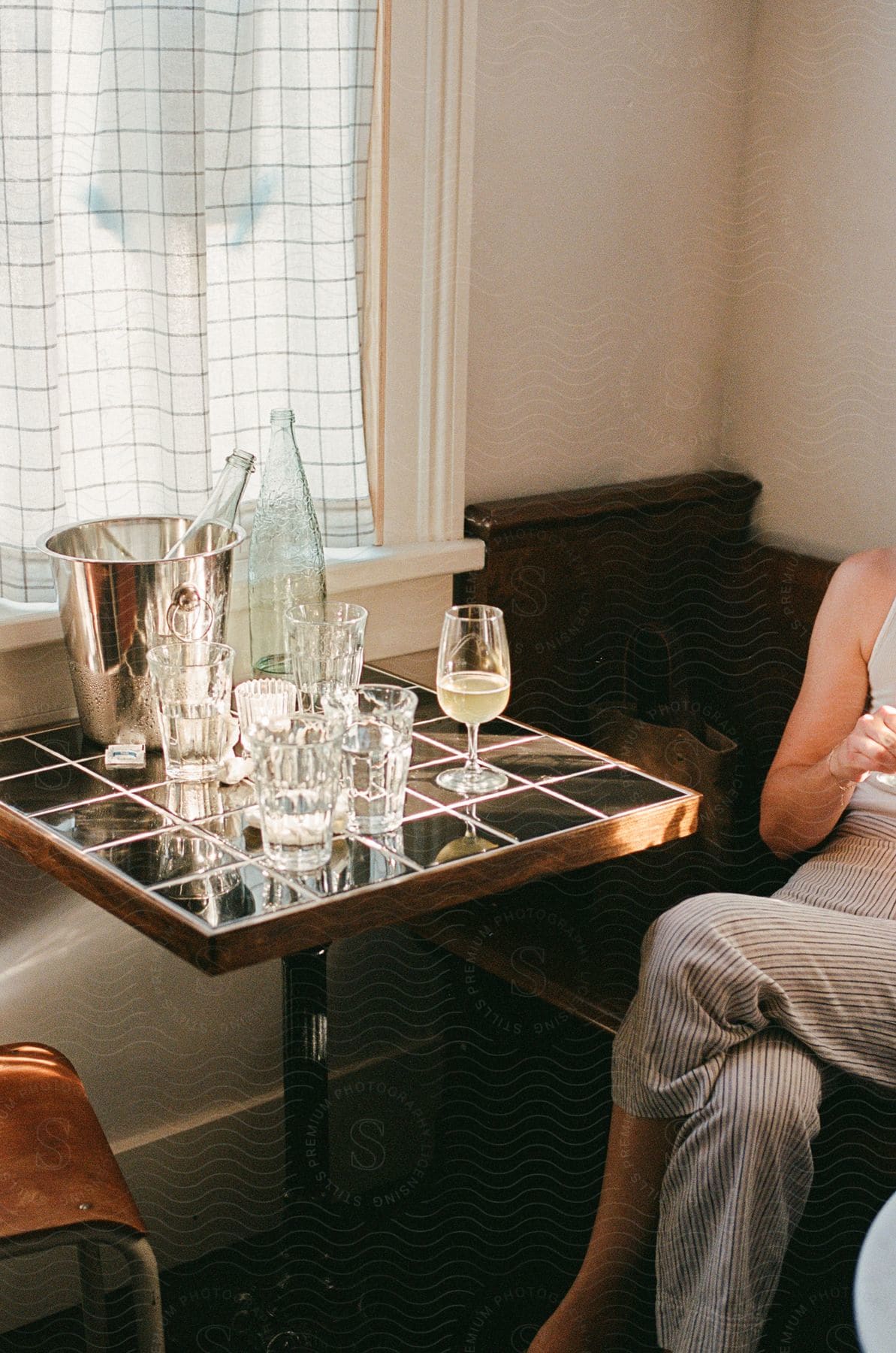 Table setting with empty glasses and a wine bottle next to a seated woman in a well-lit room.