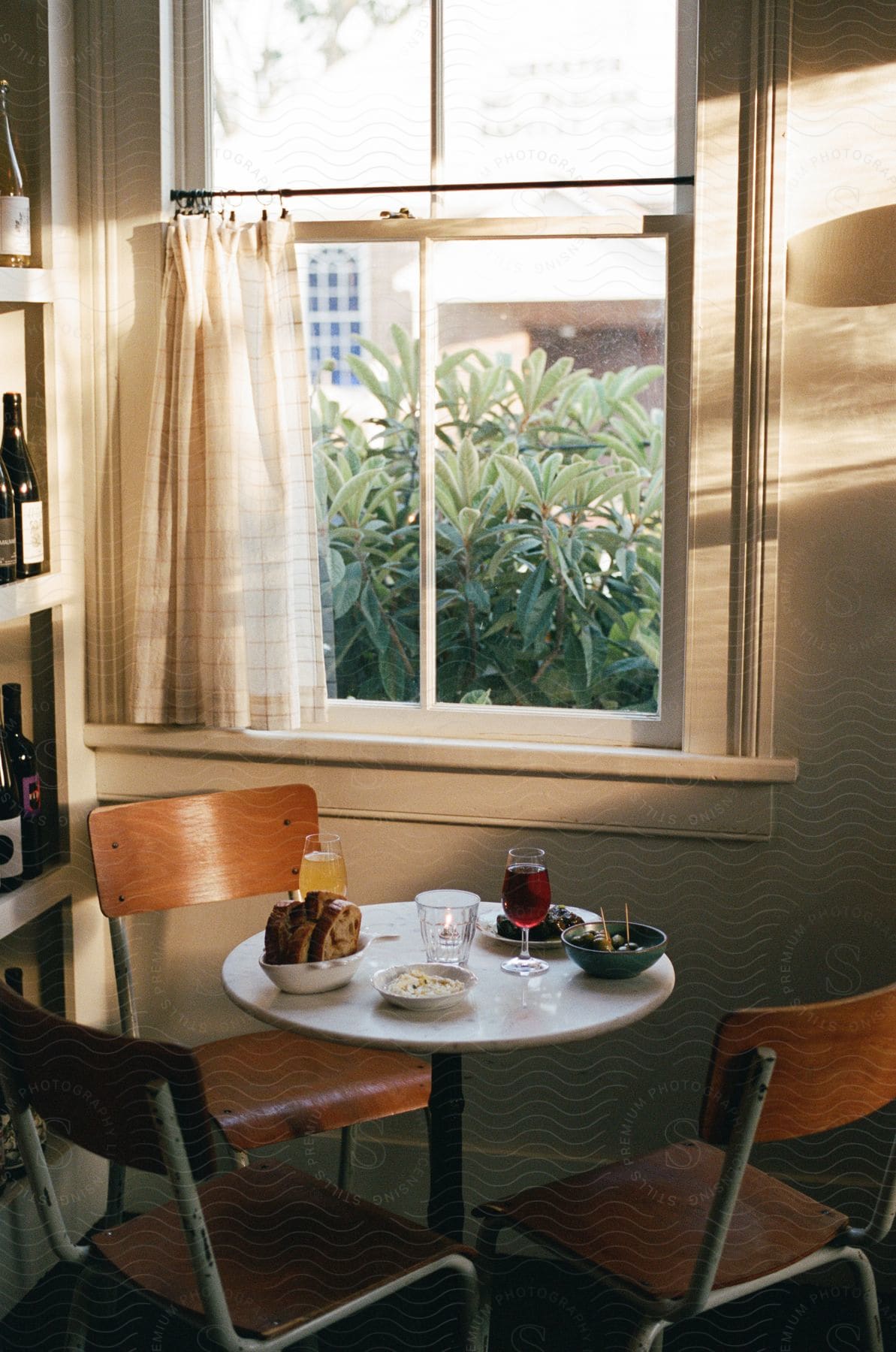 Stock photo of table set with meal  sits in corner between shelves of wine bottles and a window.