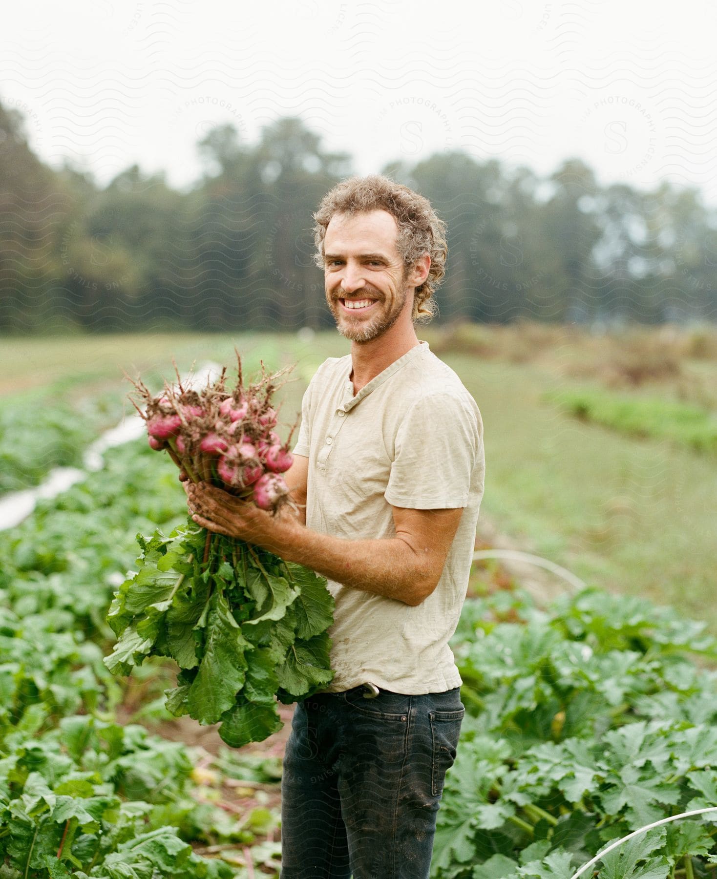 A man stands in a garden holding a bundle of radishes