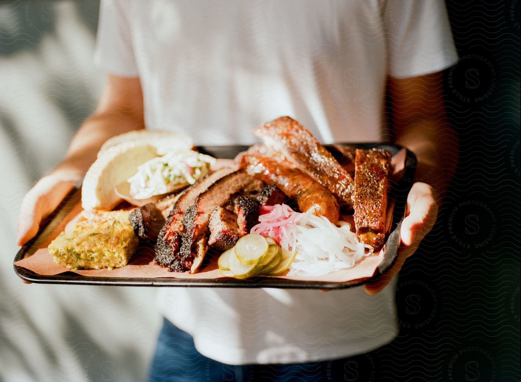Person stands holding tray ladden with a meal containing barbecued meat.