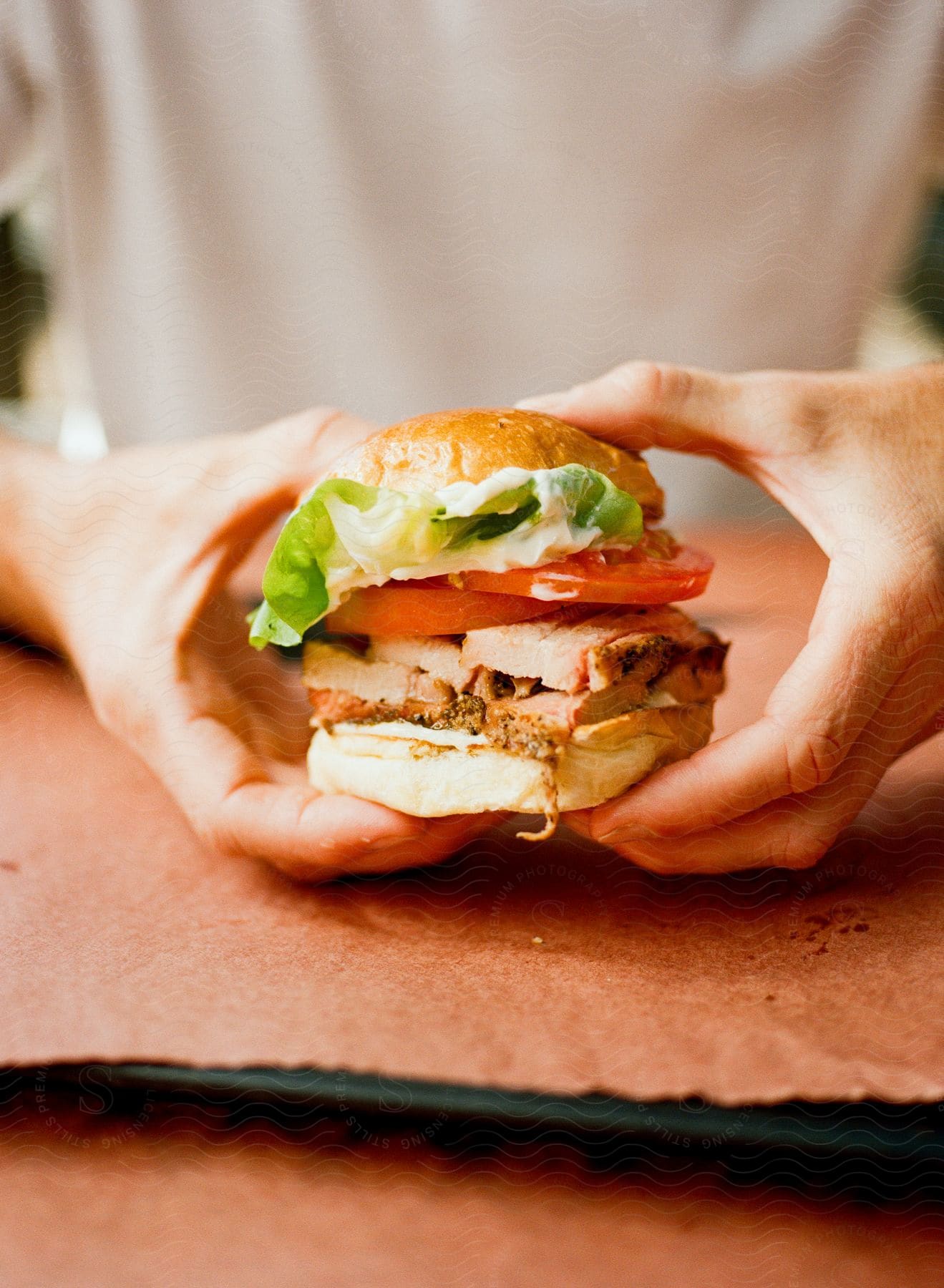 Two hands hold fully loaded sandwich with lettuce tomato meat and bun