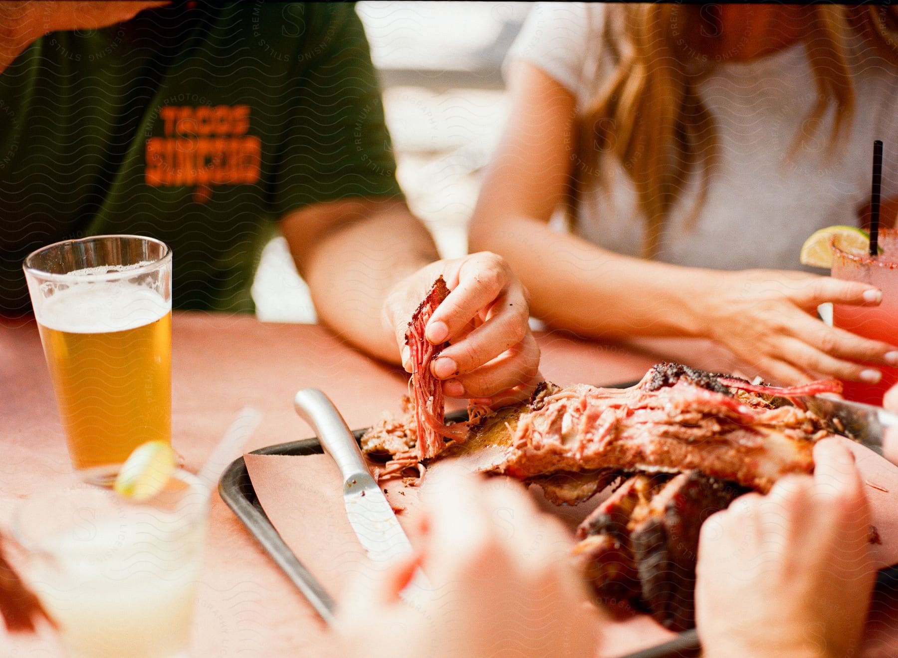 A woman holds her drink as the man sitting next to her eats ribs with a beer