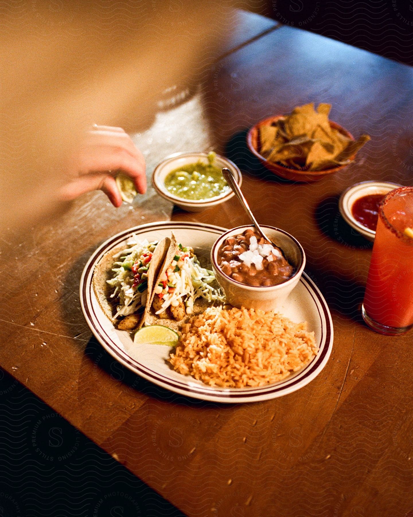 A woman's hand reaches over a table with plates of Mexican food and an iced drink