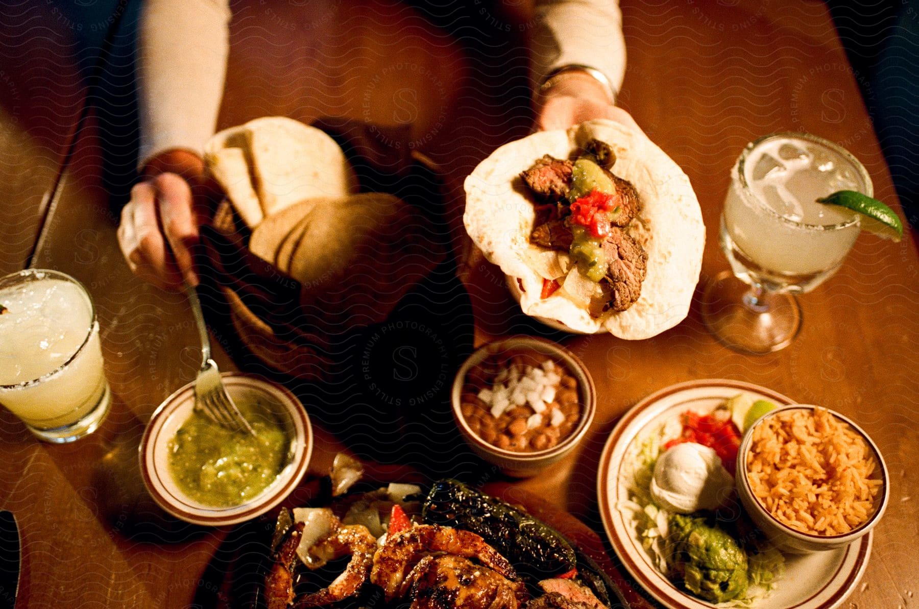 A woman with her fork in the salsa verde building her fajita with food and margaritas on the table