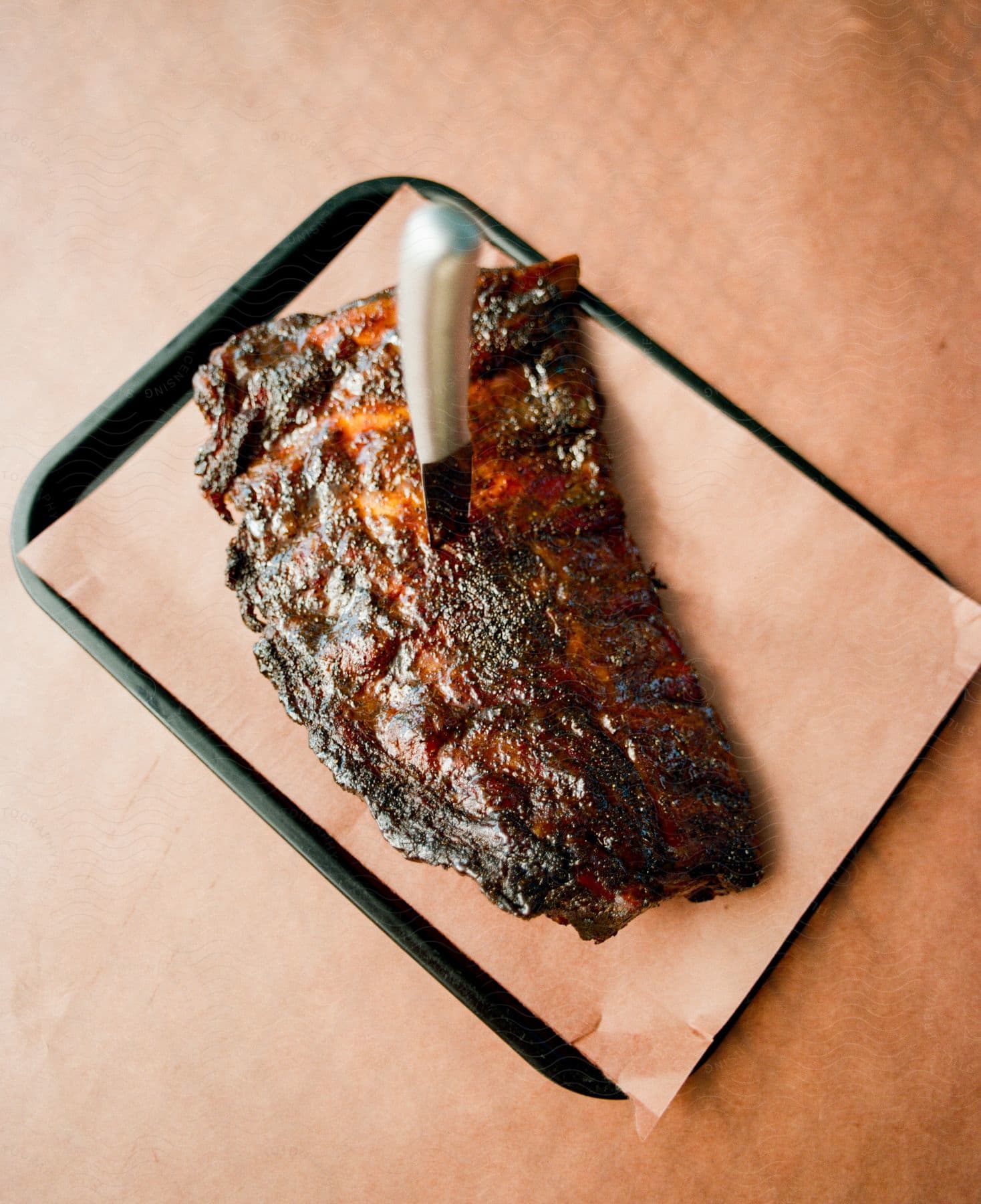 A slab of barbecue ribs sits on a tray with a knife stuck in the center.