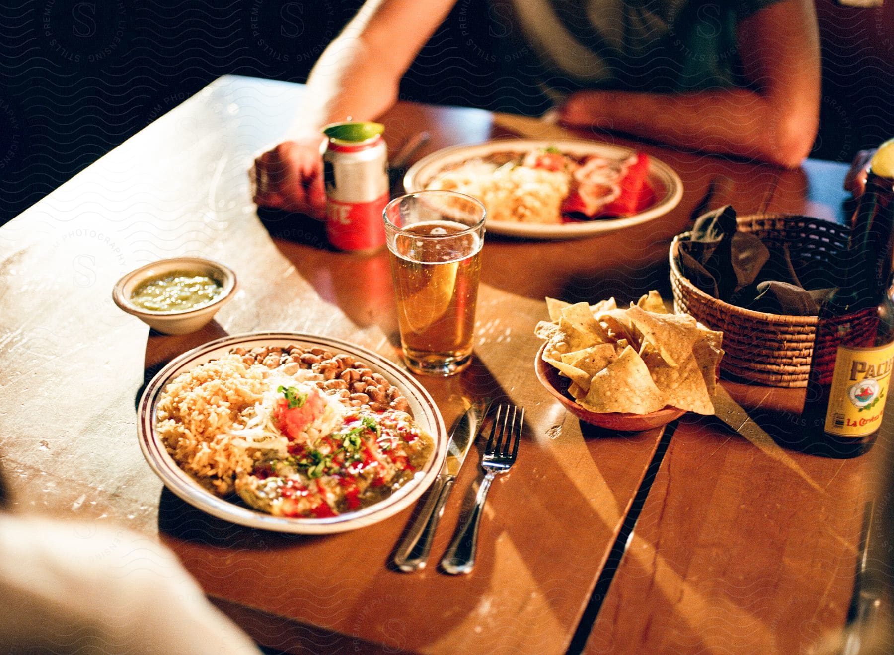 A Man Leans His Arms On A Table With Two Plates Of Food And A Glass Of Beer