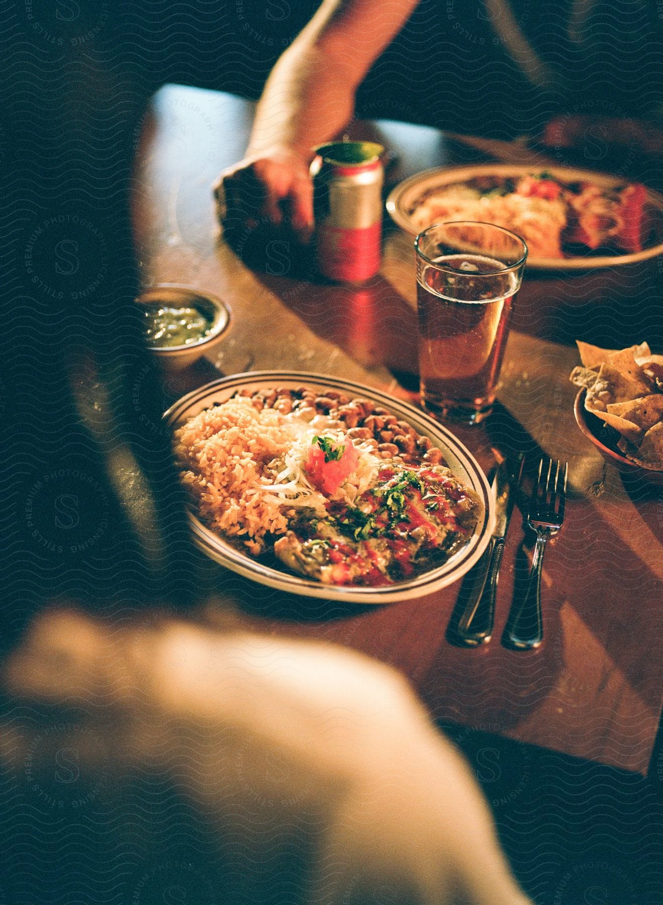 Plate of Mexican food with rice and beans, alongside a glass of beer and a can on a wooden table.