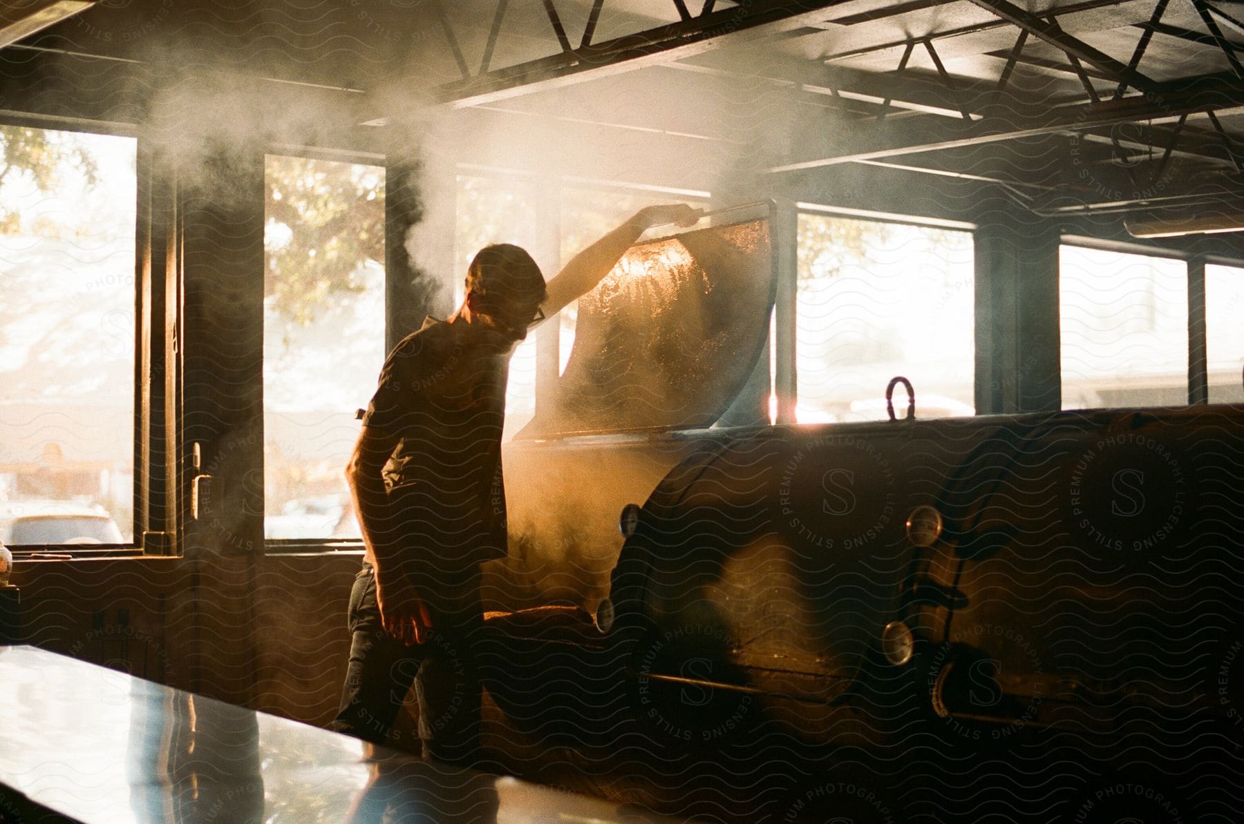 Steam rises as a man lifts the lid of an offset smoker