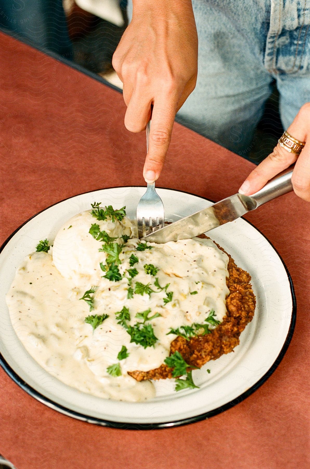 A person cutting a chicken fried steak on a plate.