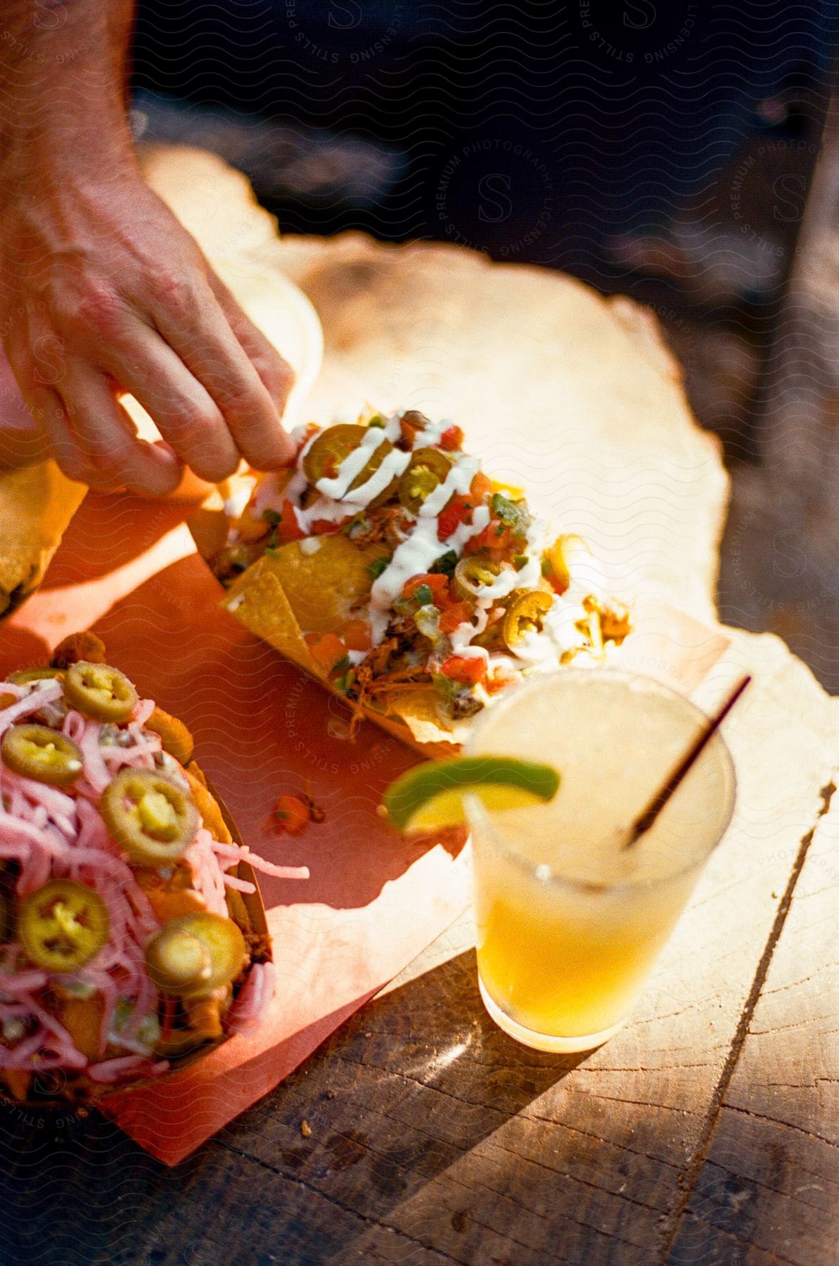 Fancy nachos covered in jalapenos on a wooden stump accompanied by an alcoholic drink garnished with lime.