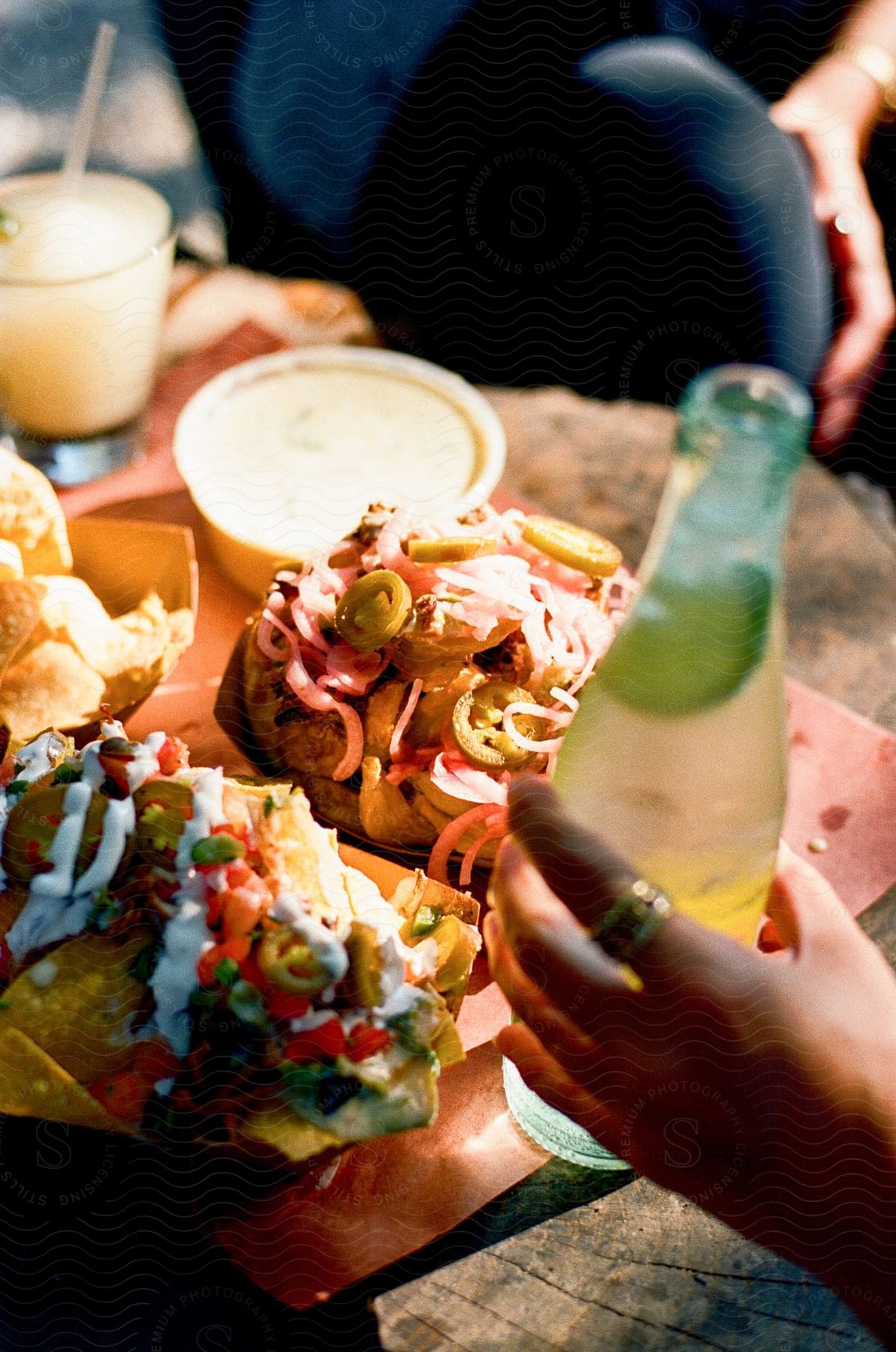 A person holds a bottle of alcohol while sharing nachos with another person.