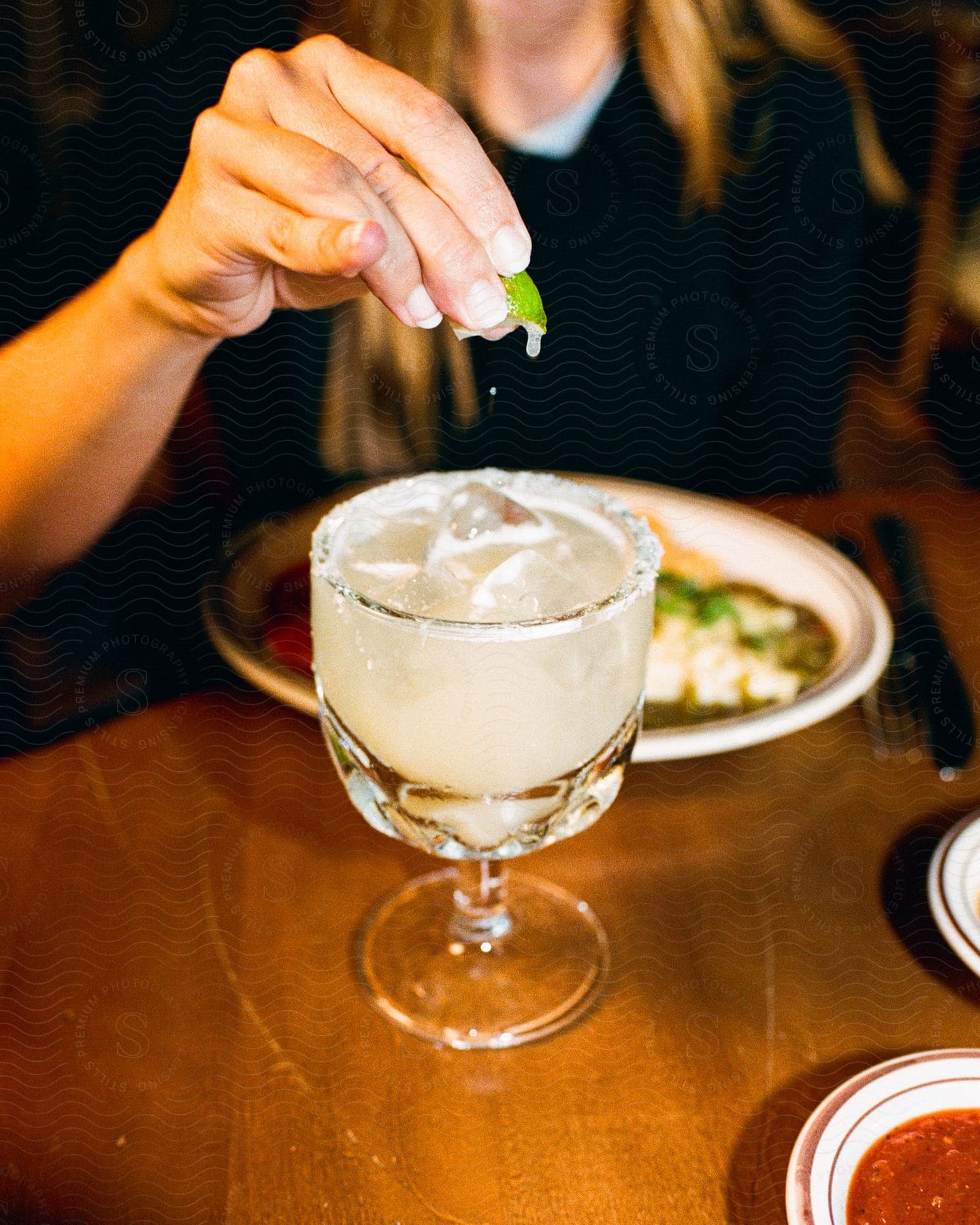 A woman squeezes lime into her drink as she sits at a table with her meal
