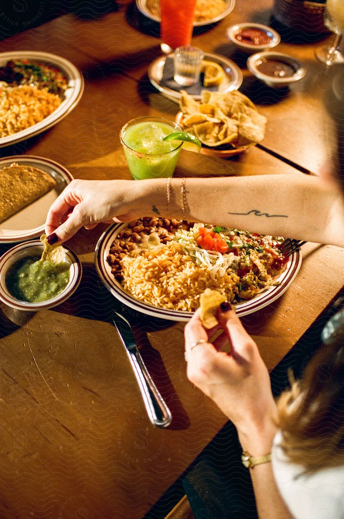 A woman is sitting at a dining table filled with food and drink as she eats