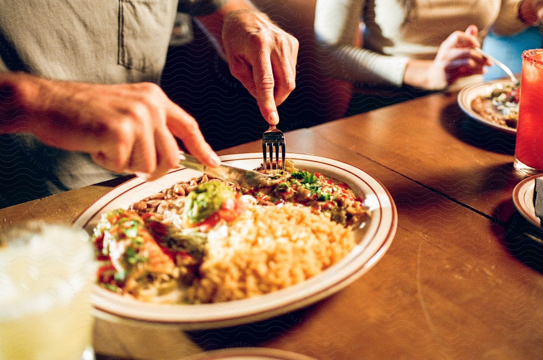 Stock photo of a man holds a knife and fork as he sits at a table and eats