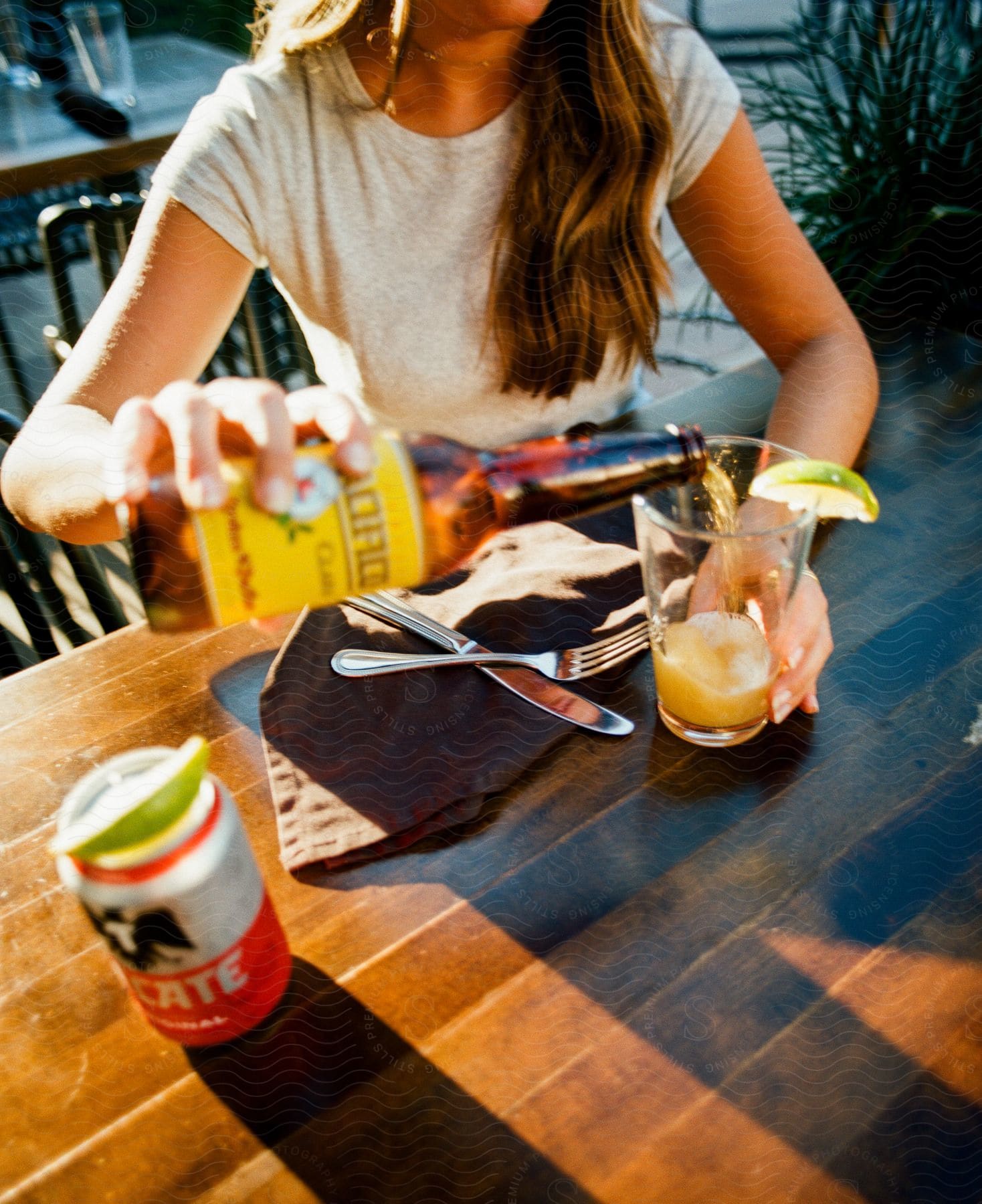 Stock photo of a woman is sitting and pouring beer that is in the bottle into a glass with a lemon on the edge of the glass