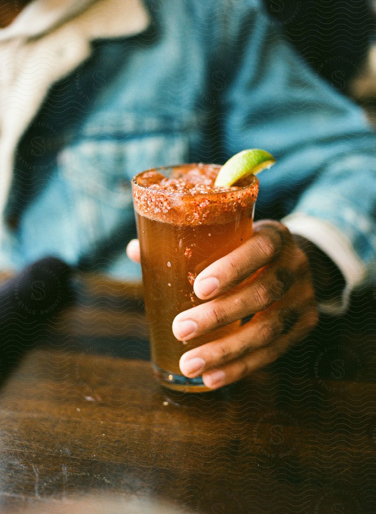 Man holding a glass rimmed with spice and garnished with lime, filled with a reddish beverage.
