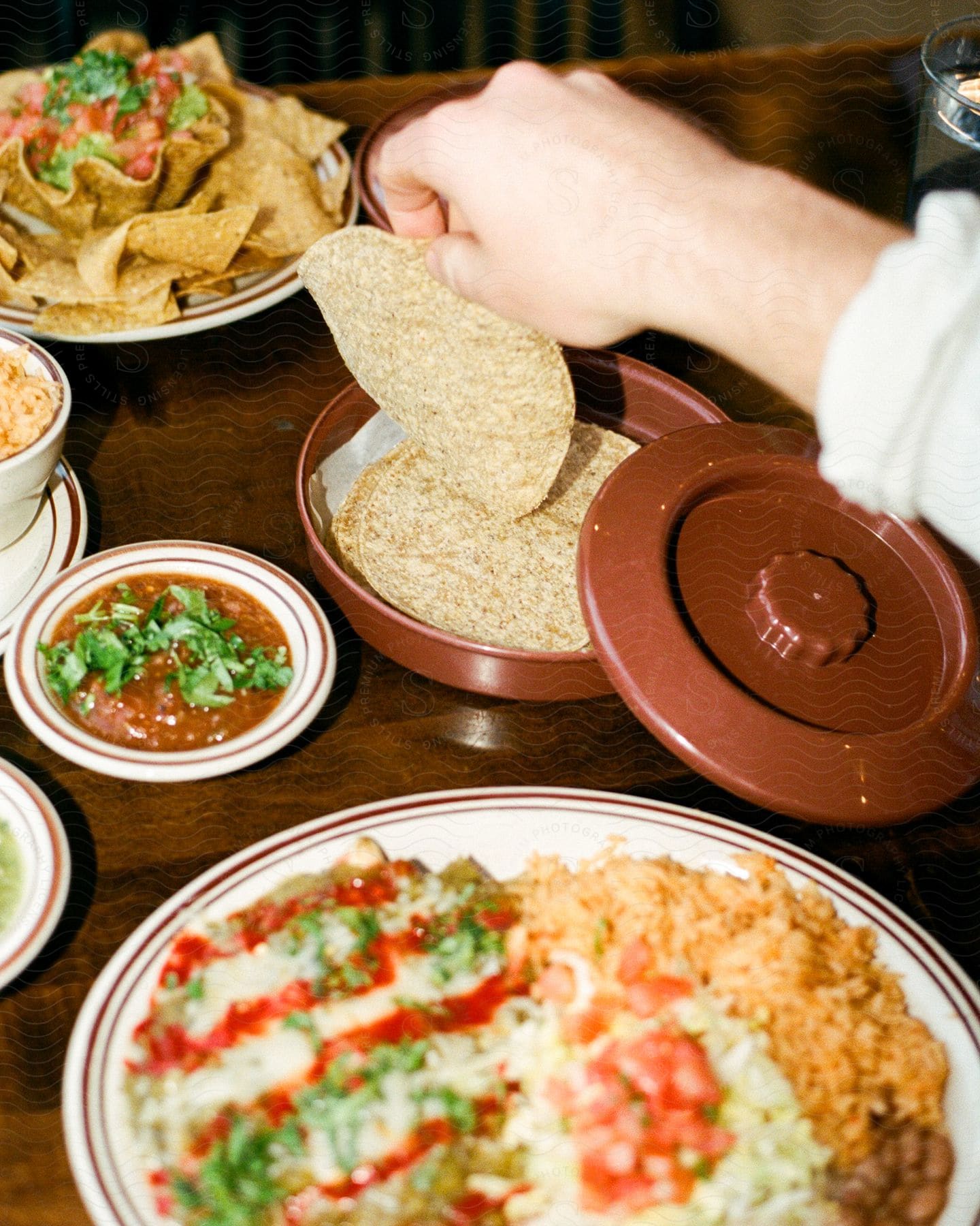 A man reaches for a tortilla on a table filled with Mexican food