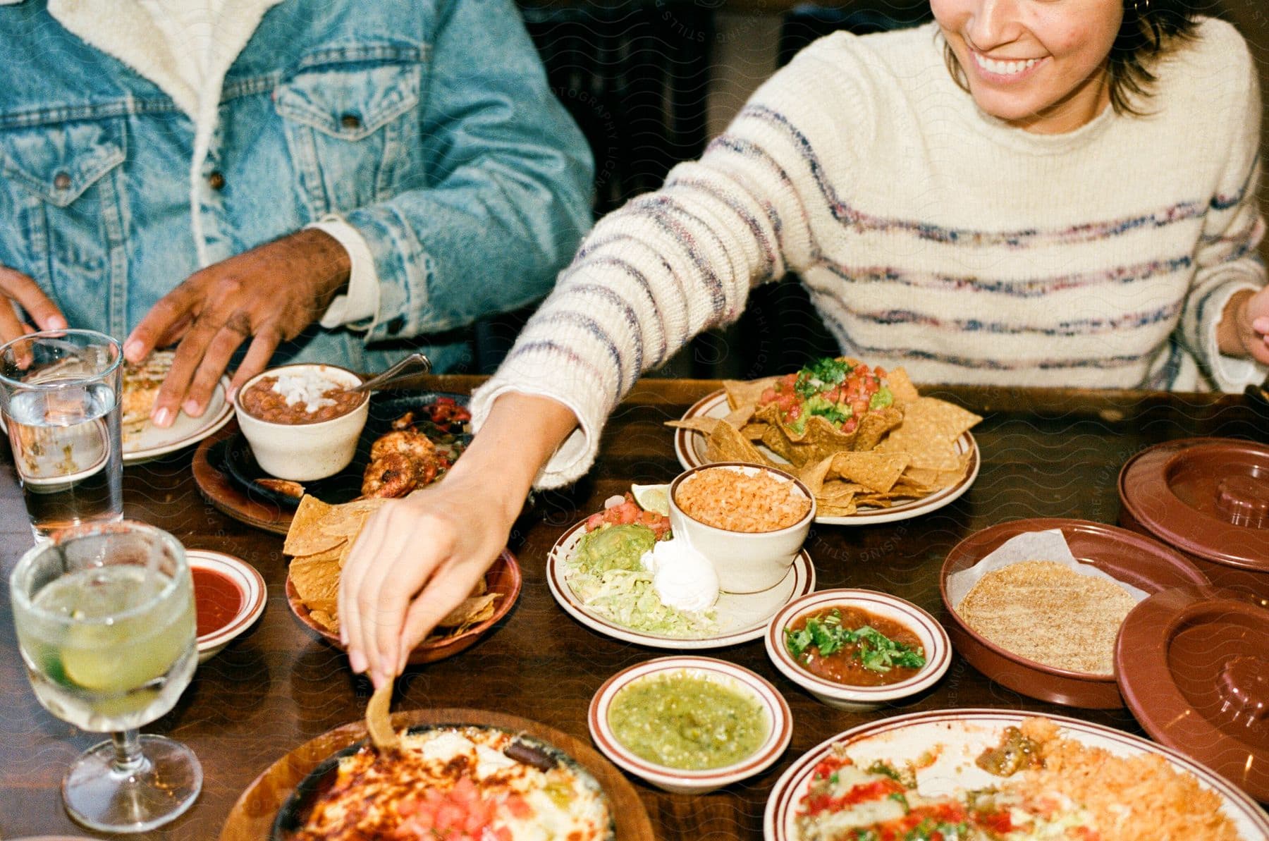 A woman smiling as she dips her chip into one of the many mexican dishes on the restaurant table