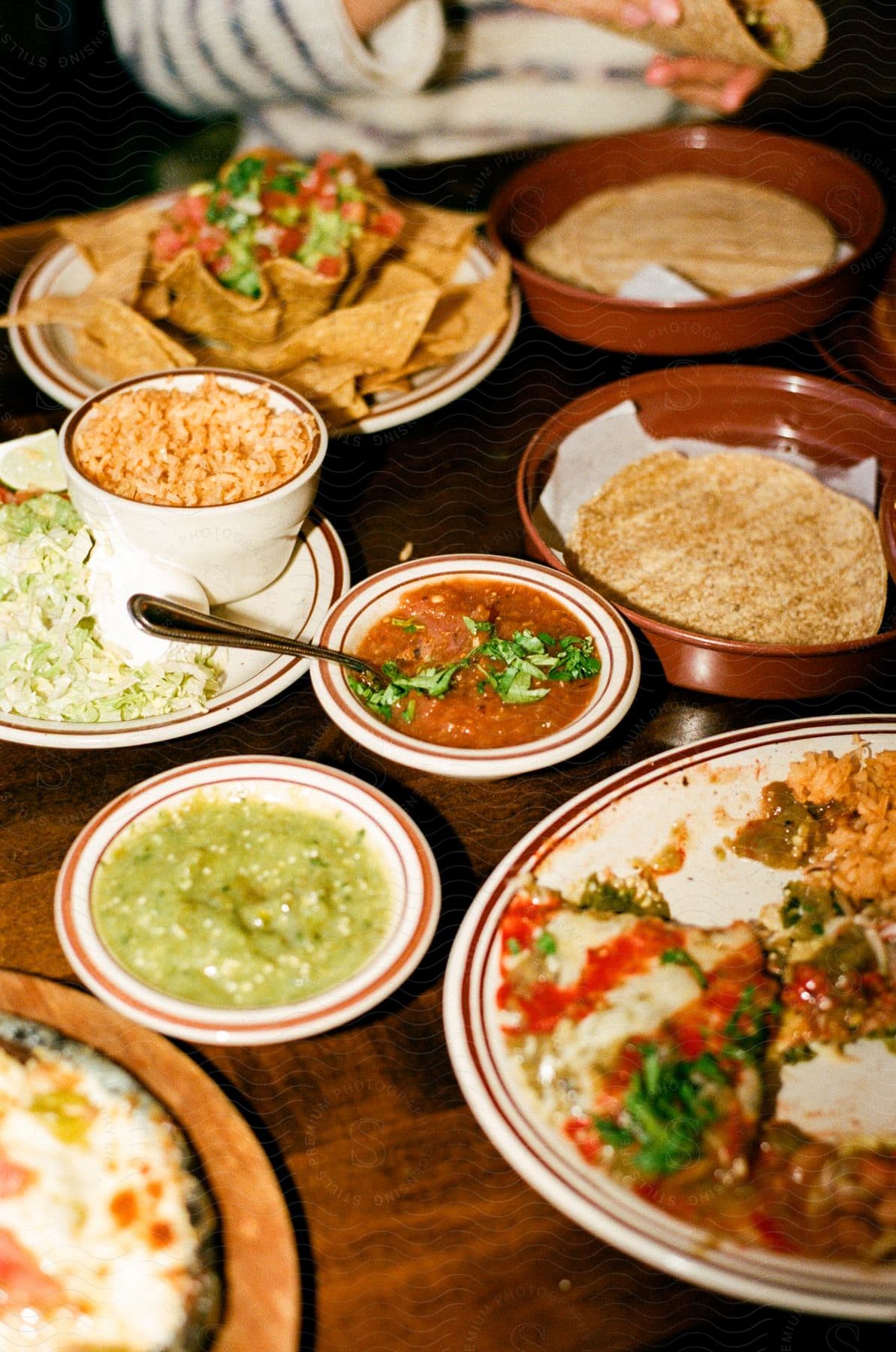 Plates and bowls of Mexican food fill a table as someone sits in the distance