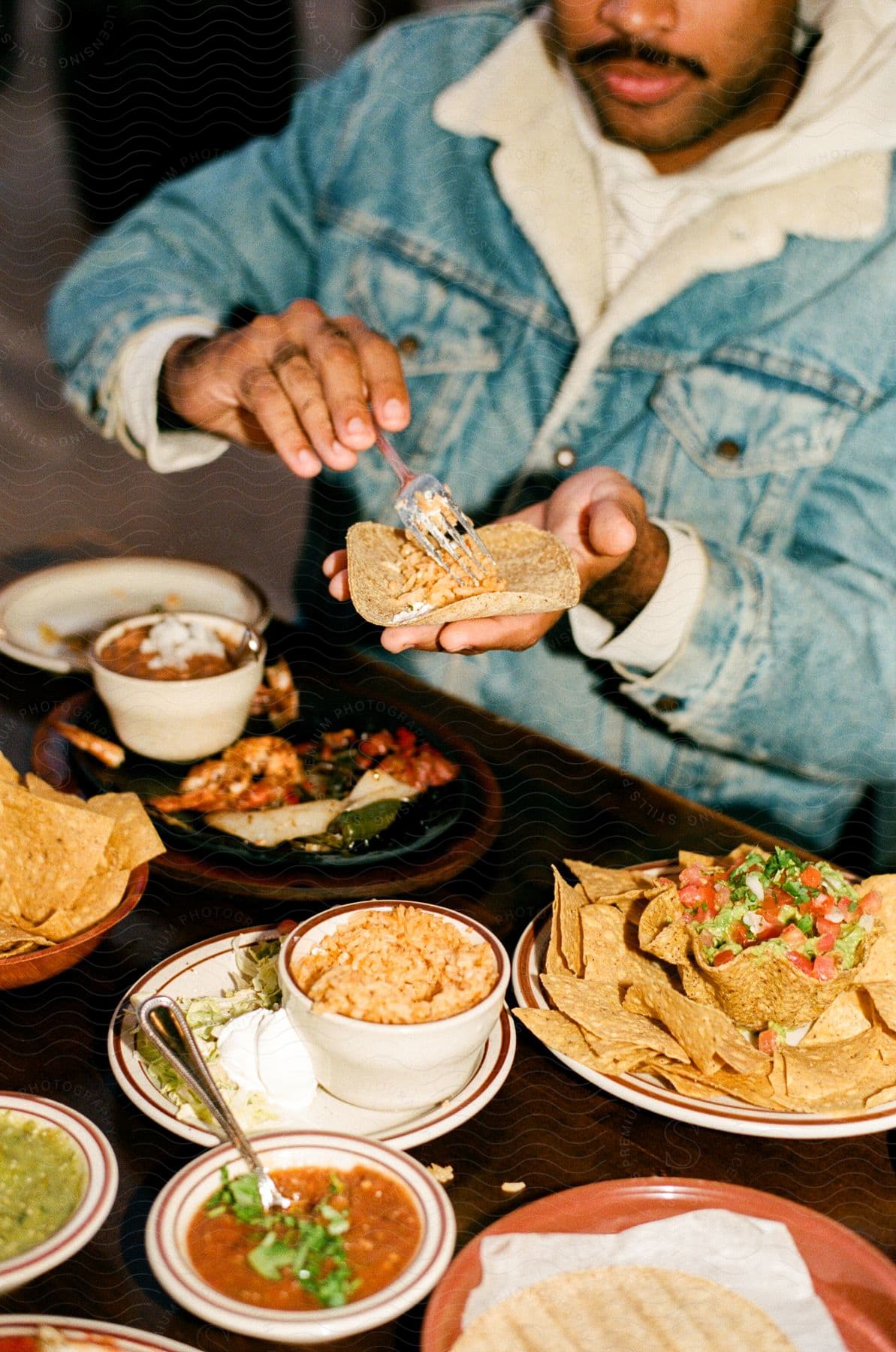 Man seasoning a taco over a table set with various Mexican dishes.