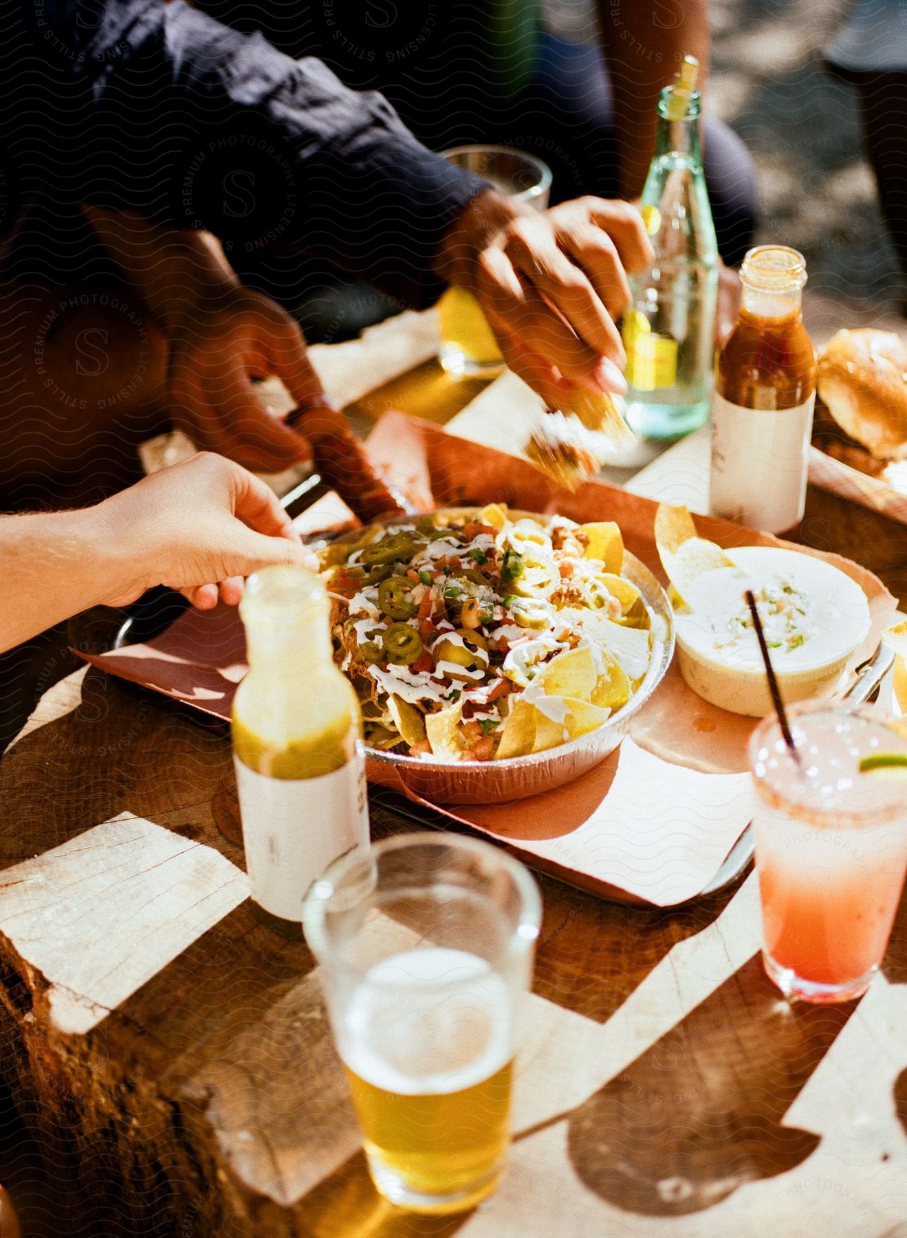 A small group of people are drinking and eating nachos in an outdoor setting.