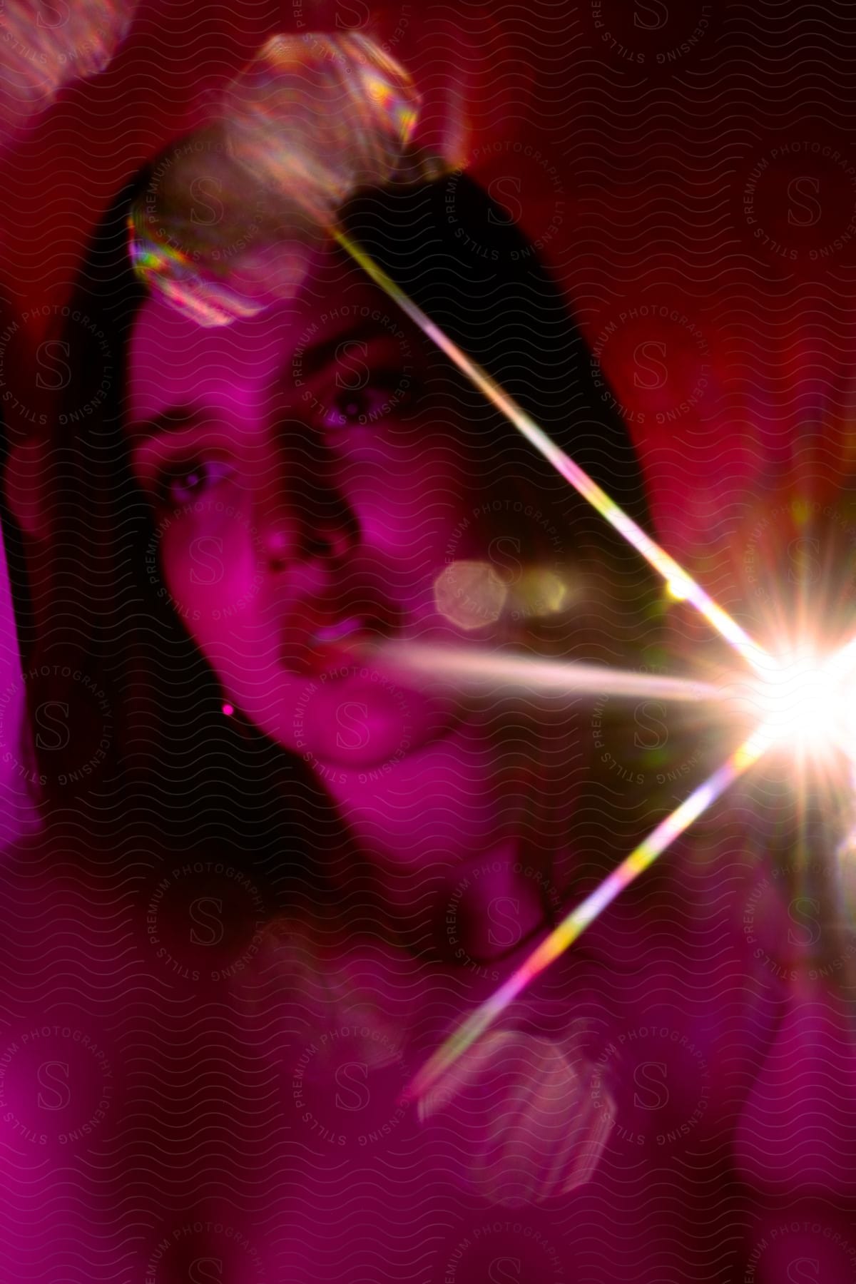 Pink light shines on a woman's face with a bright burst of light rays in the distance