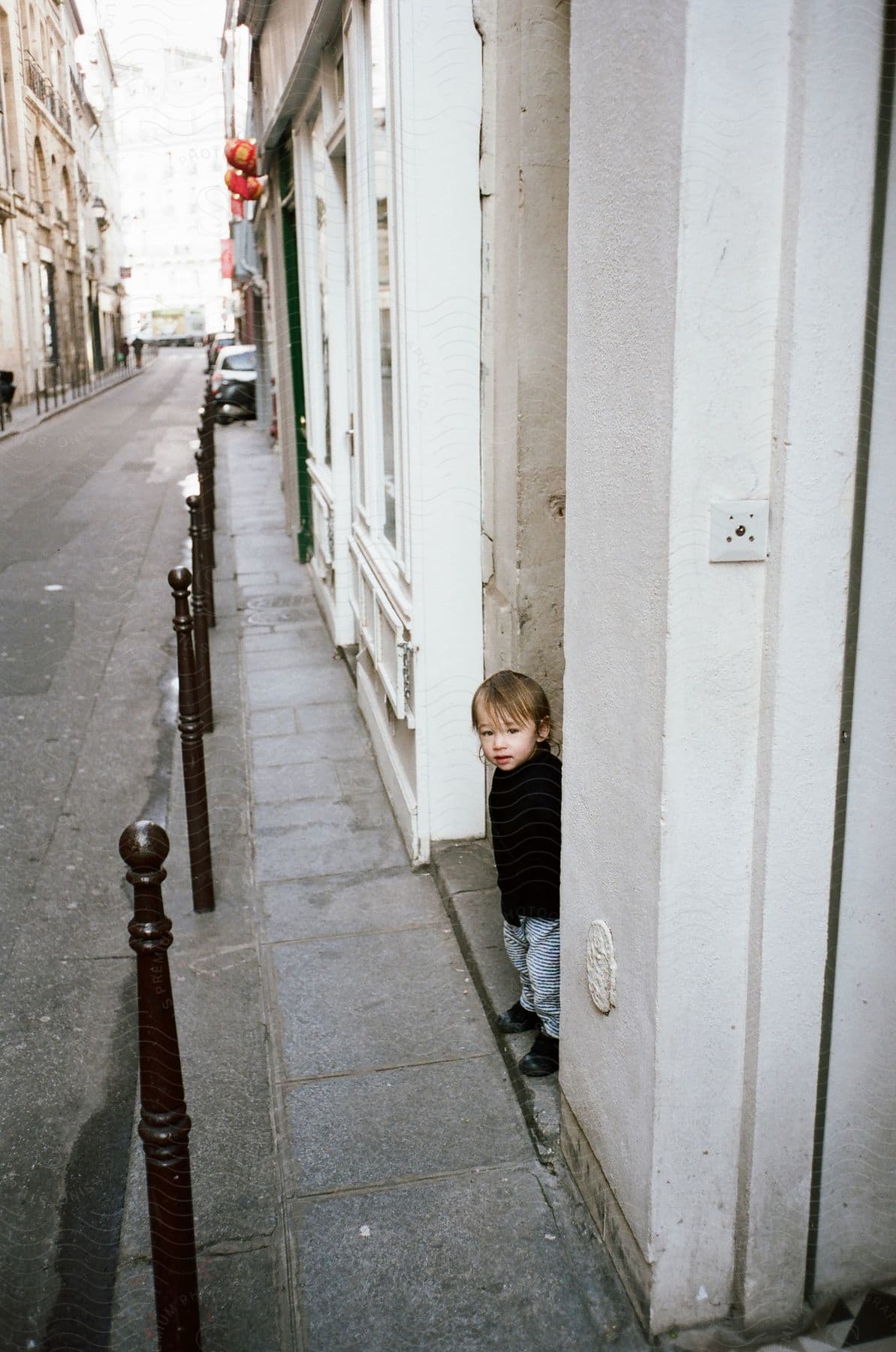 Buildings line a narrow street as a little boy stands in a doorway near the sidewalk
