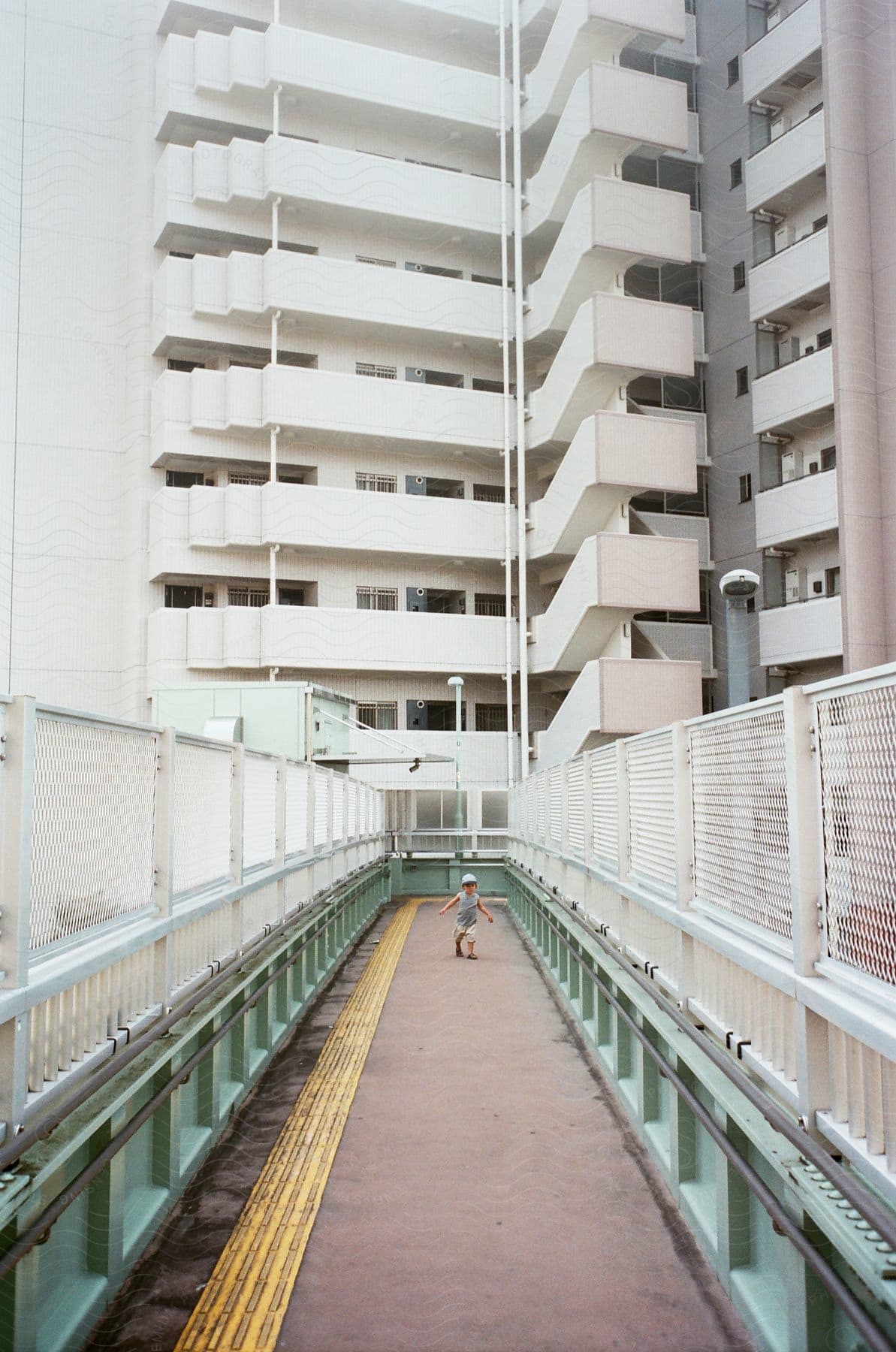 A little boy walking on a condominium bridge during the day.