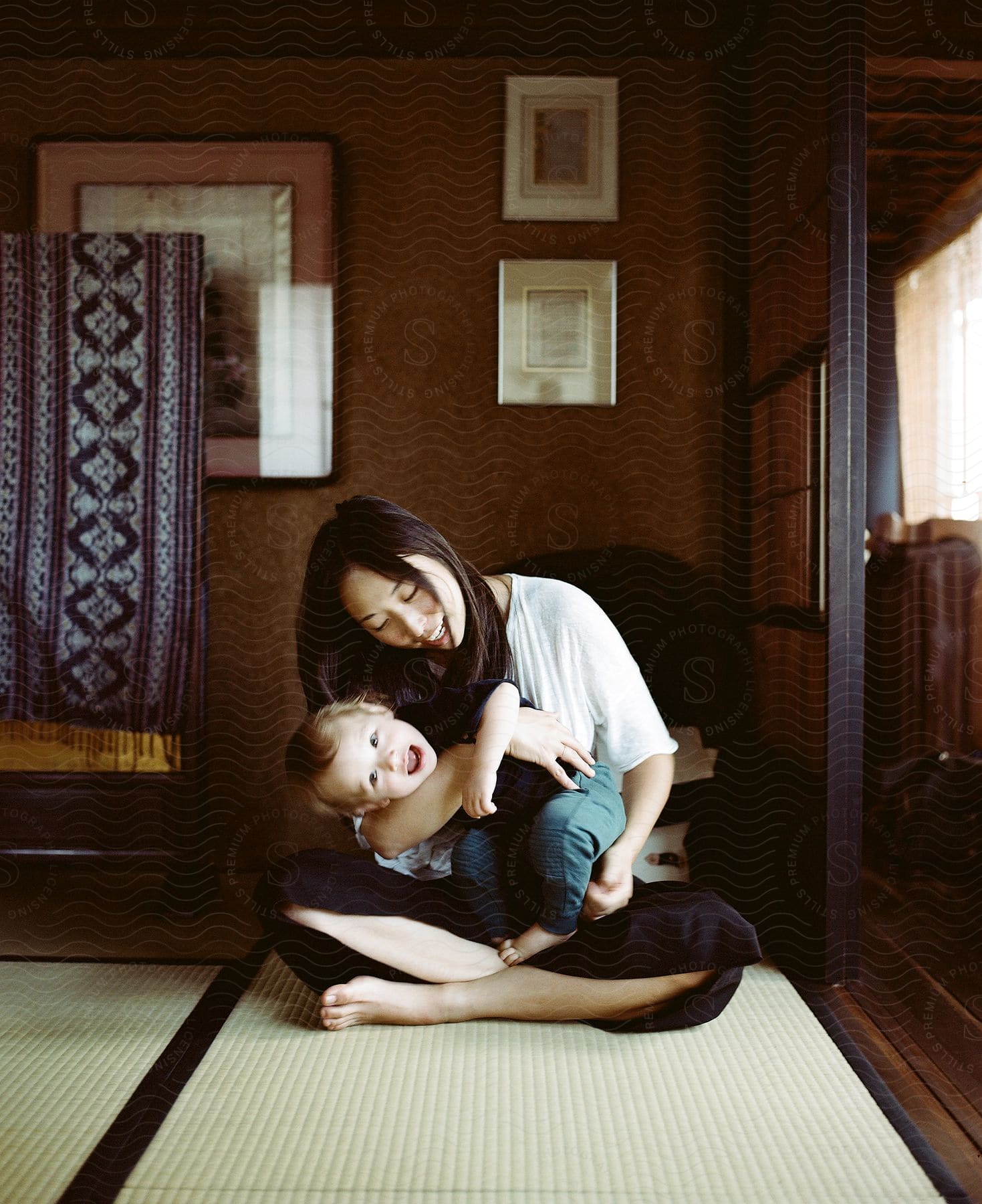 A woman cross legged on the floor, holding and playing with a laughing baby.