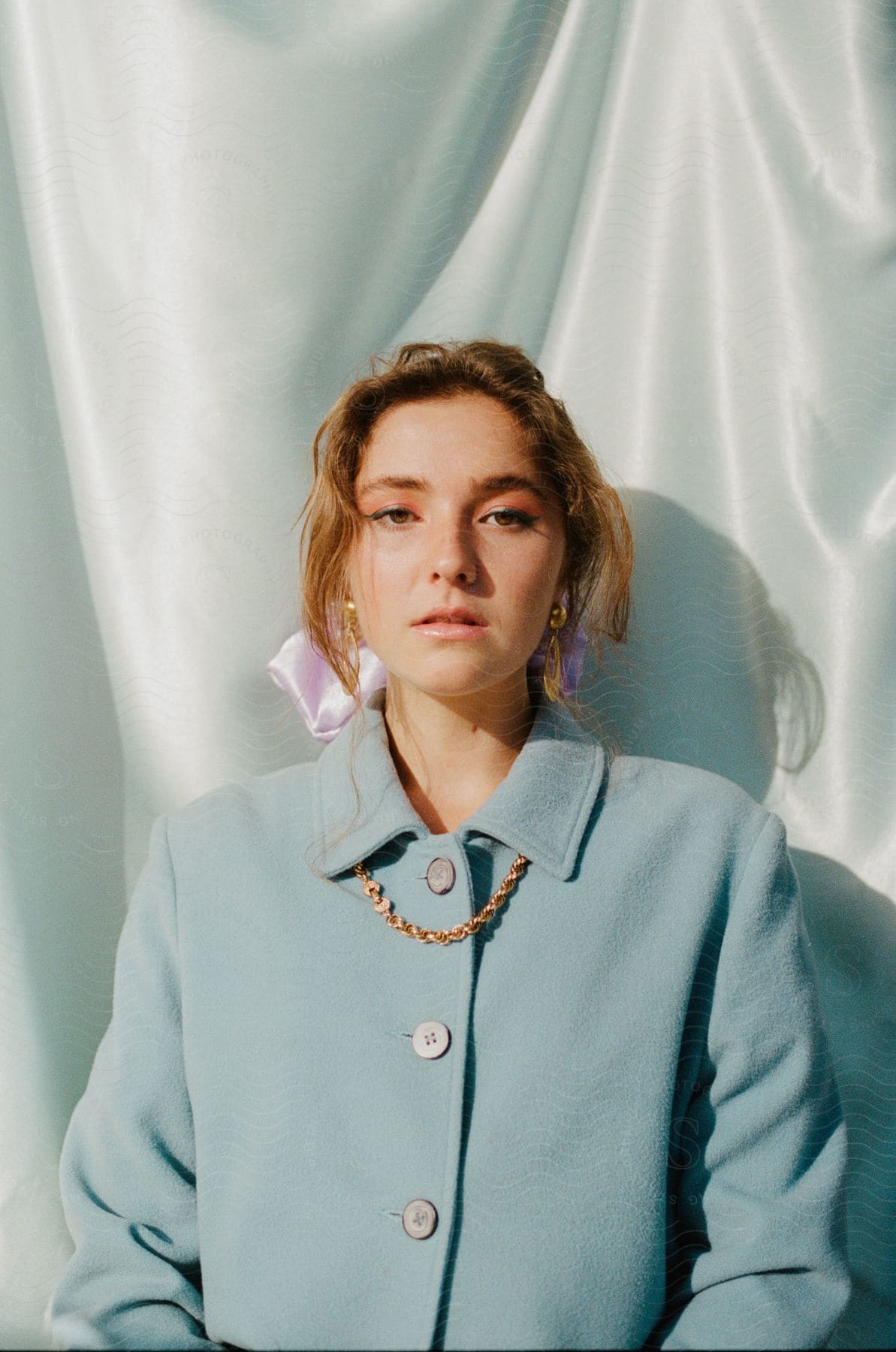 Woman wearing fashionable blue outfit casts shadow against pale fabric backdrop.