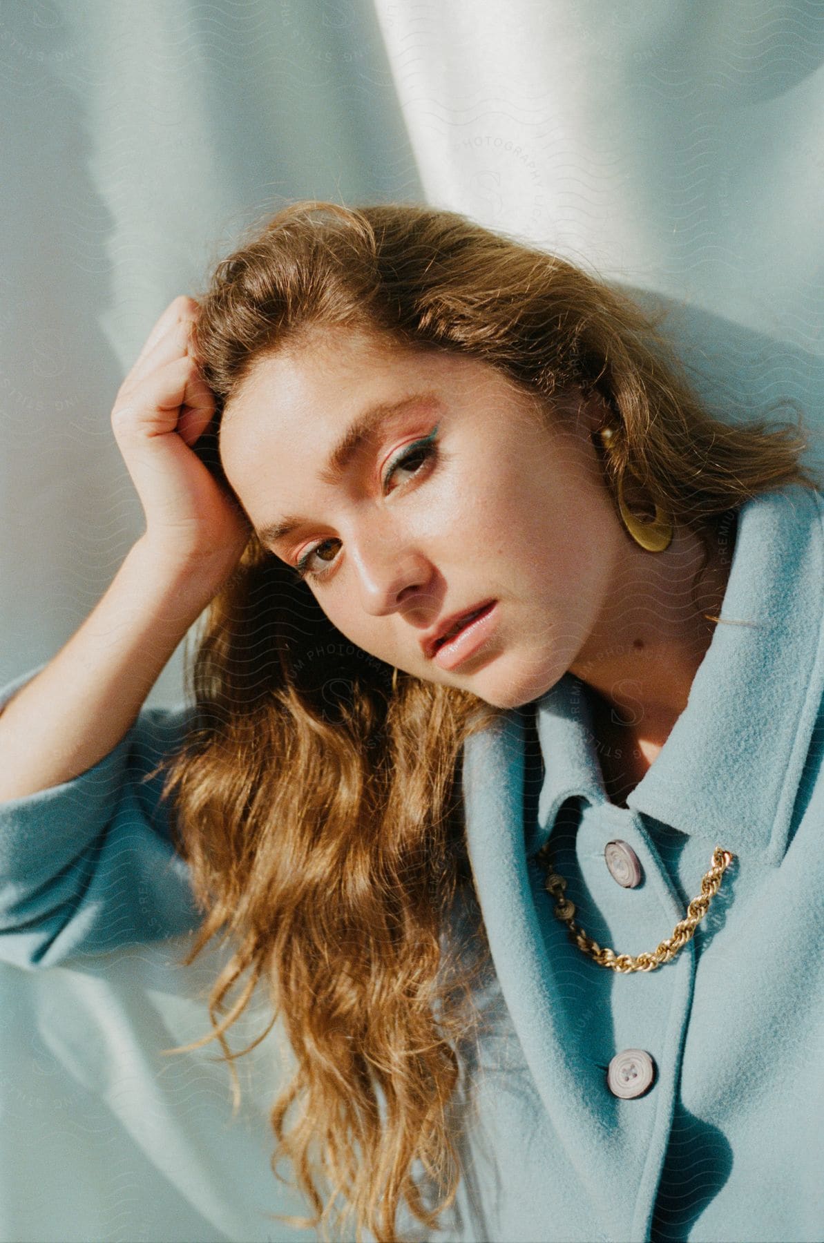 A young woman with long brown hair poses in a light blue coat.