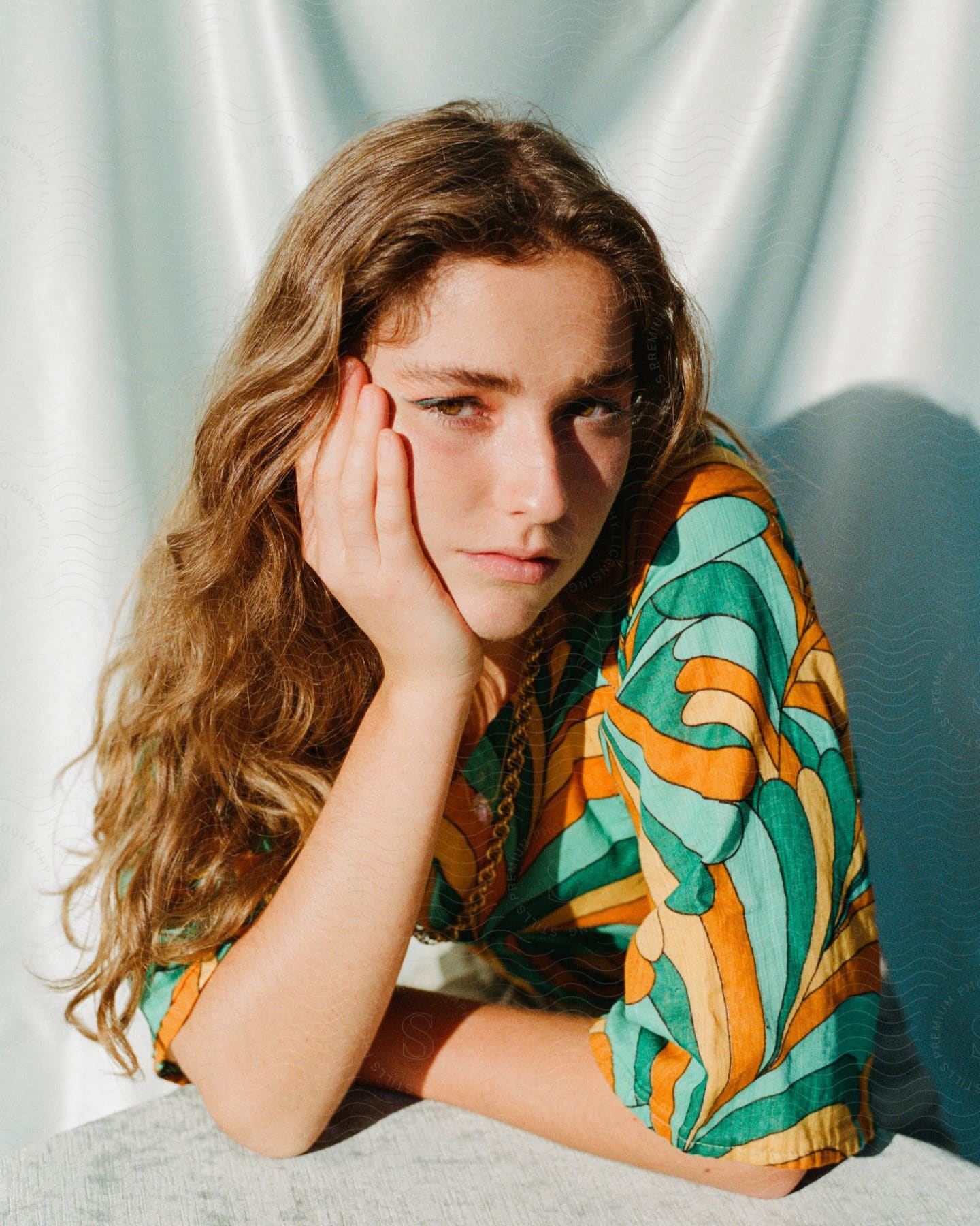 woman with light brown hair and a colorful top poses with her cheek in hand