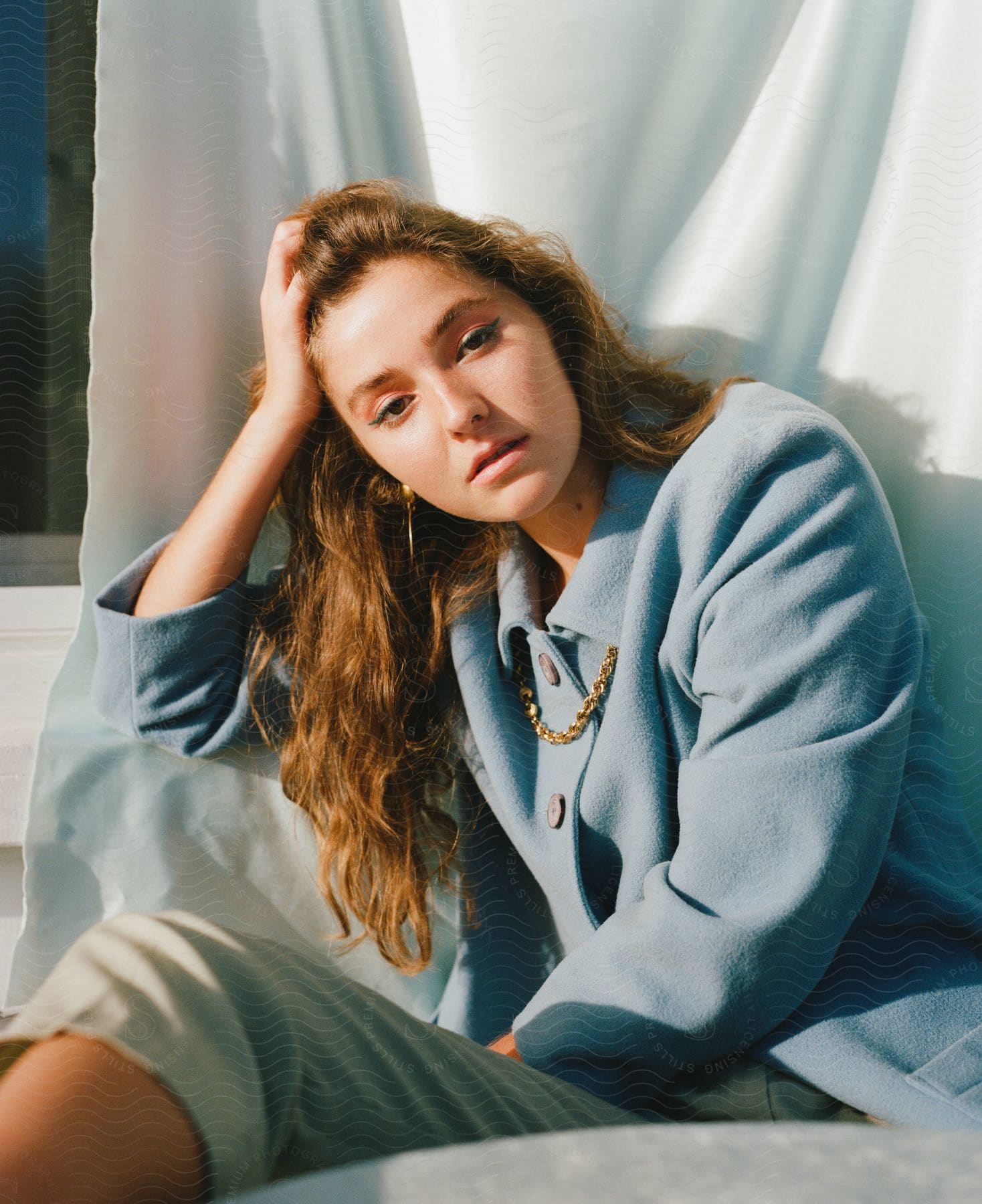 A young woman posing is sitting and is holding her head with her hand