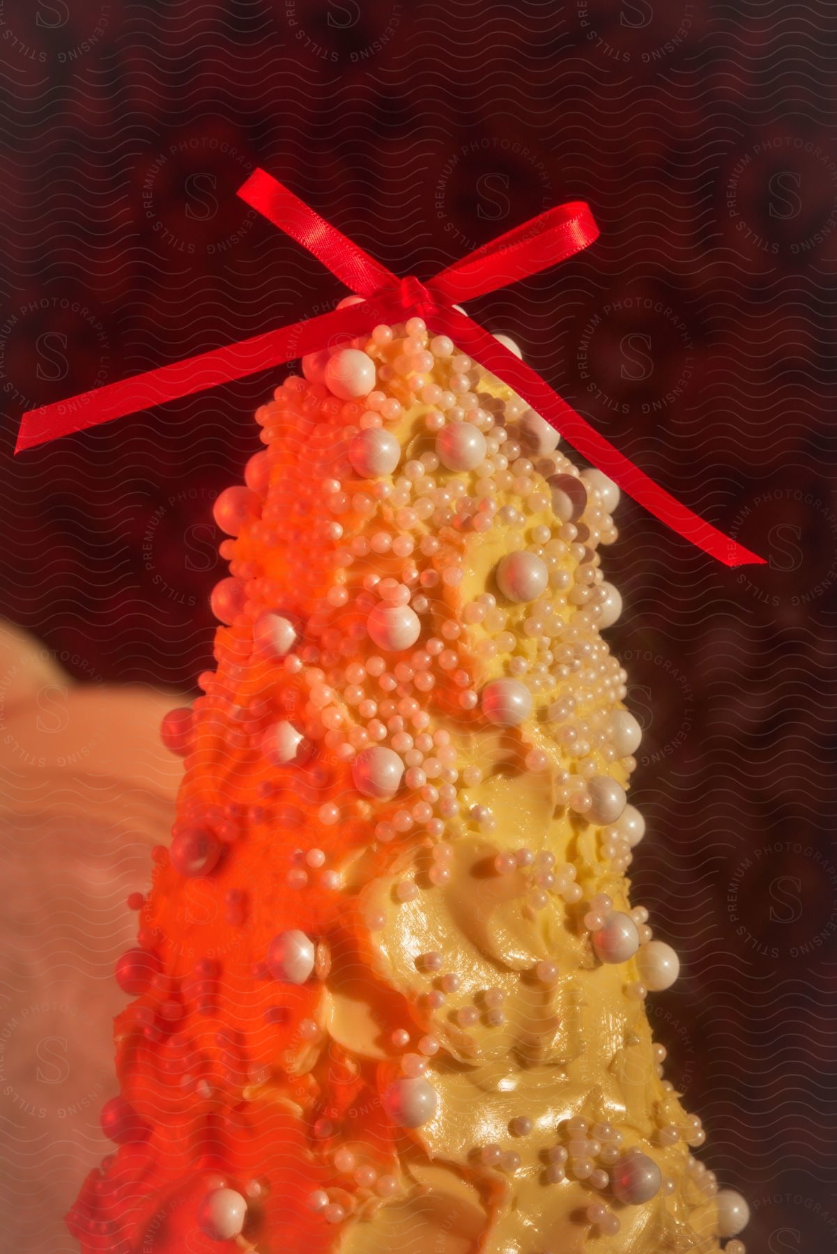 Vertical pastry with a red bow, orange frosting and candy pearls