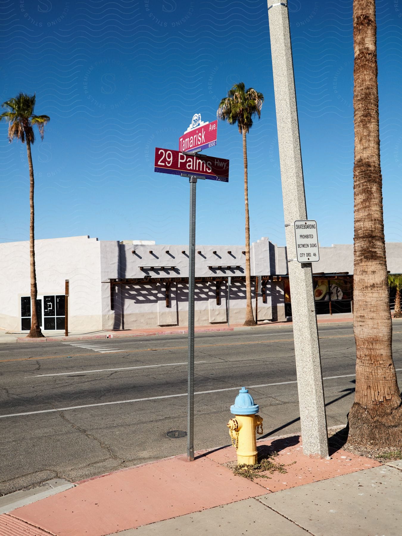 Street corner with '29 Palms Hwy' sign, palm trees, and fire hydrant on a sunny day.