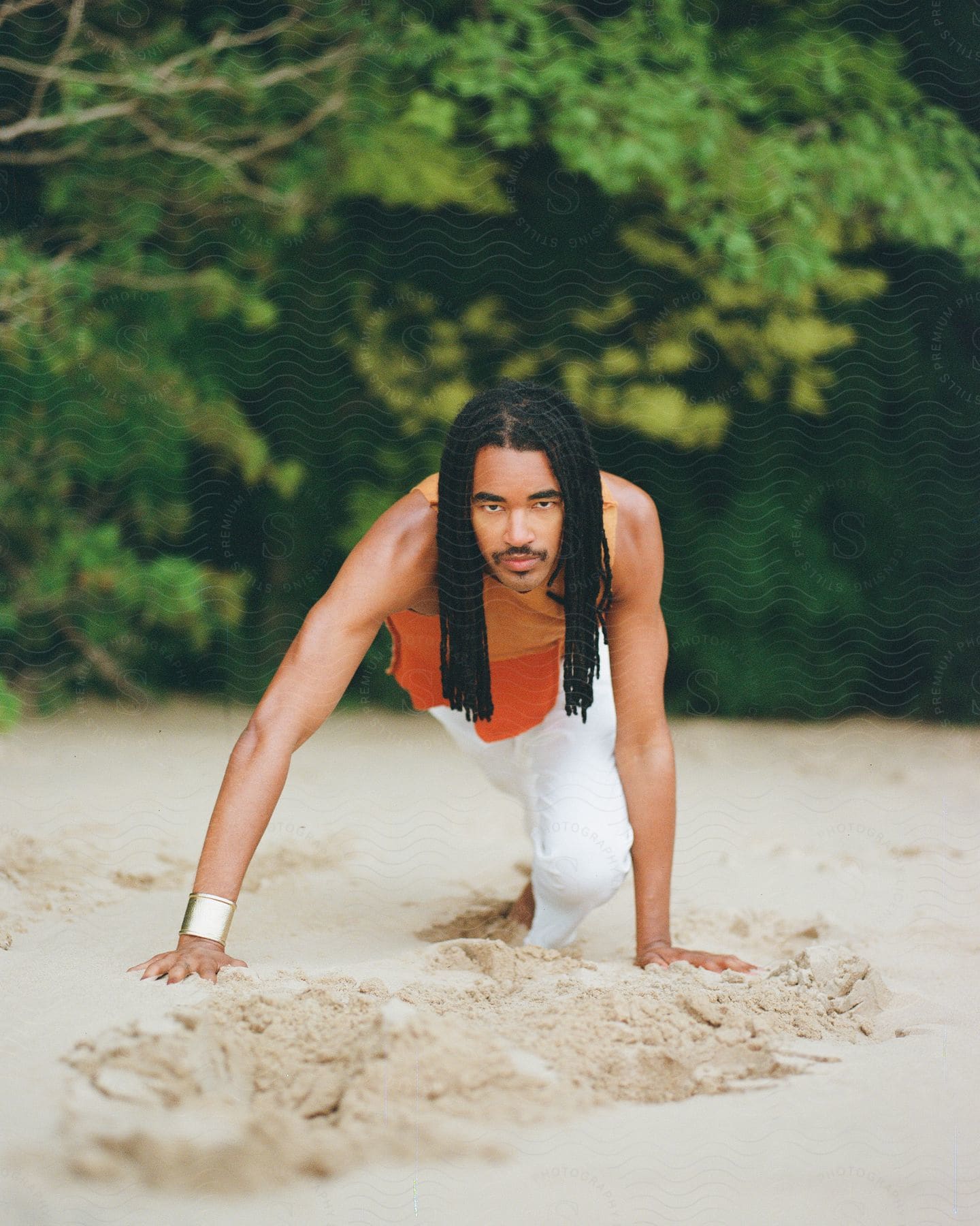 A man crouches in the sand on the beach during the day.