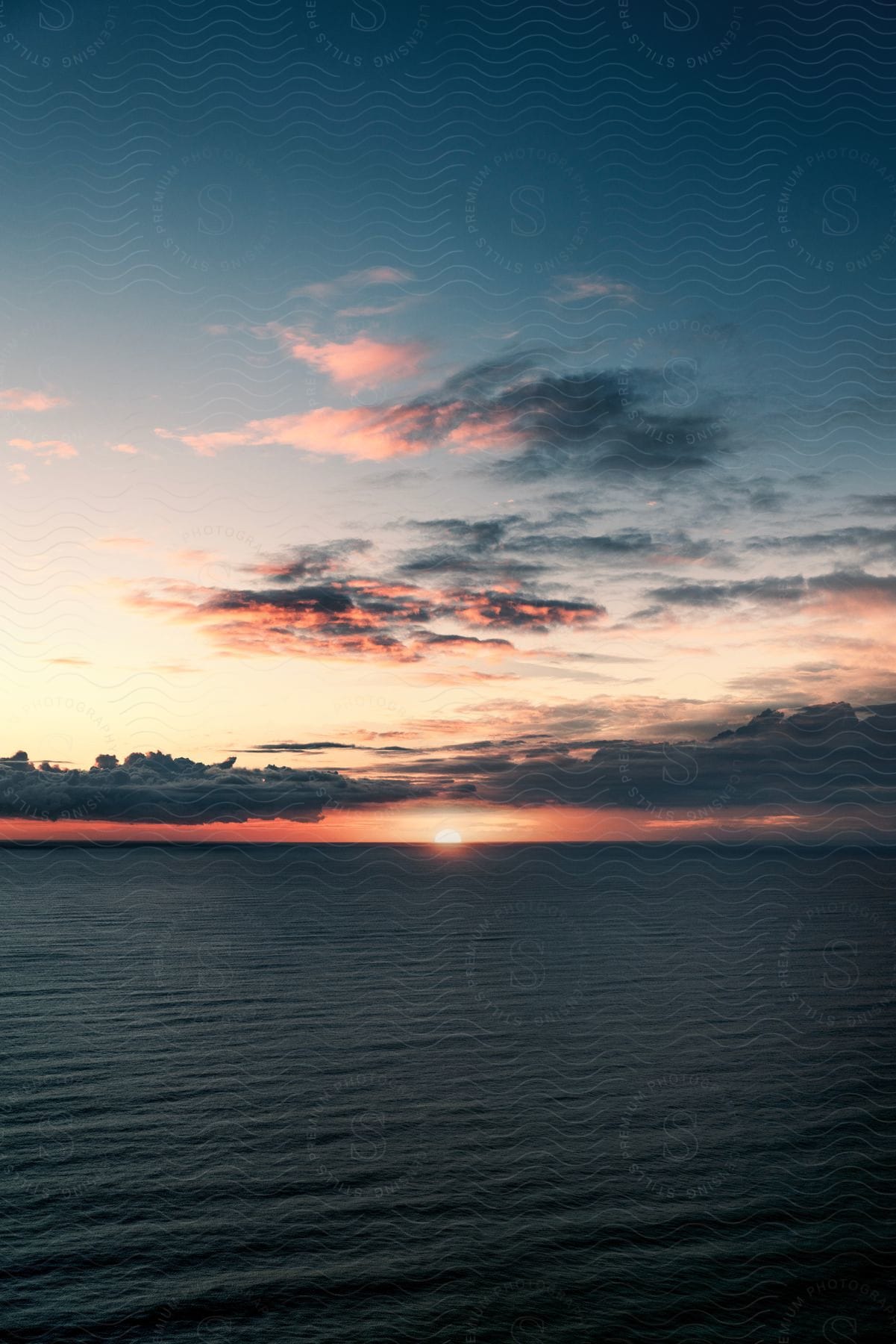 Clouds float over the water as the sun glows on the horizon