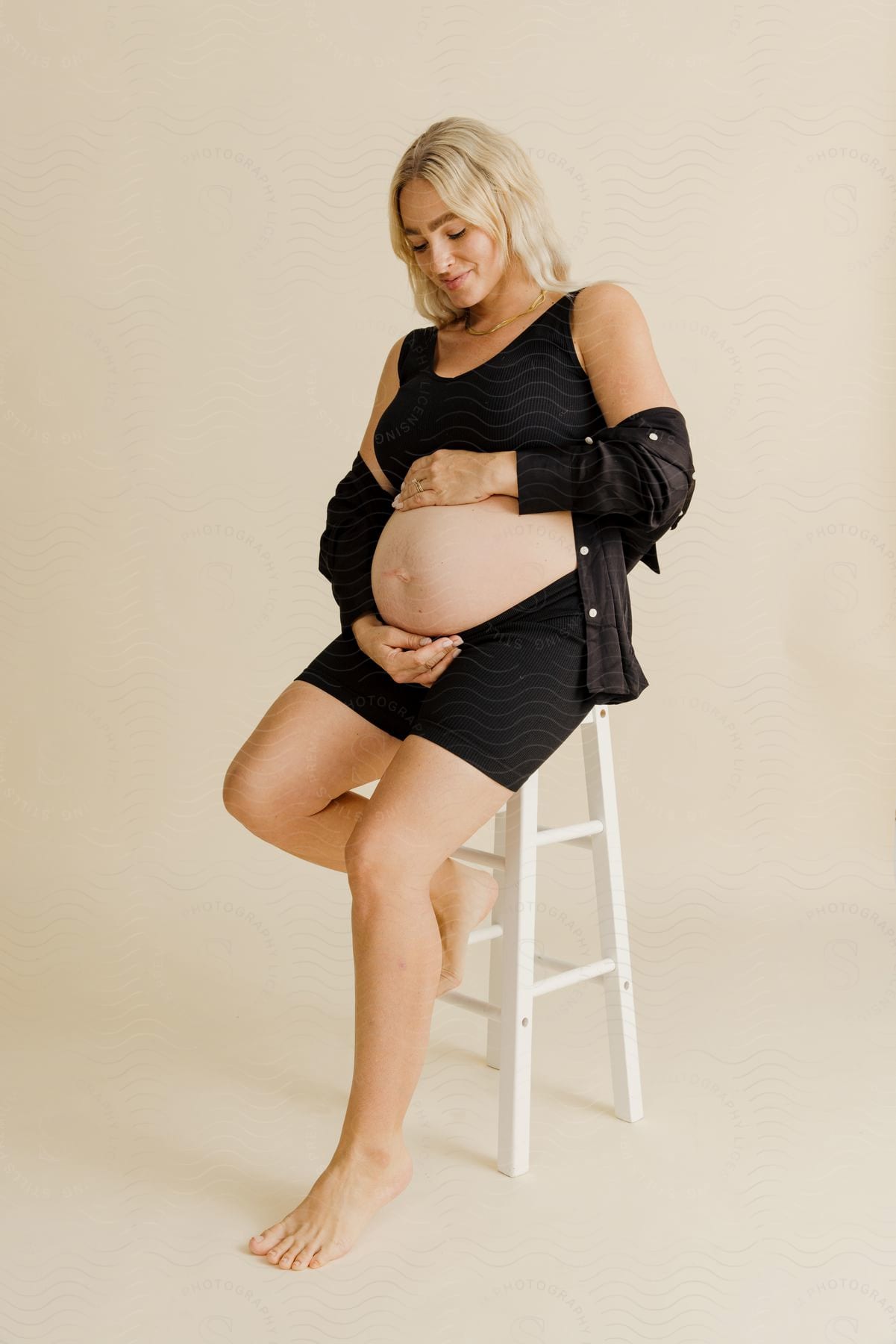 a pregnant woman sitting on a stool as she rub her hands on her belly