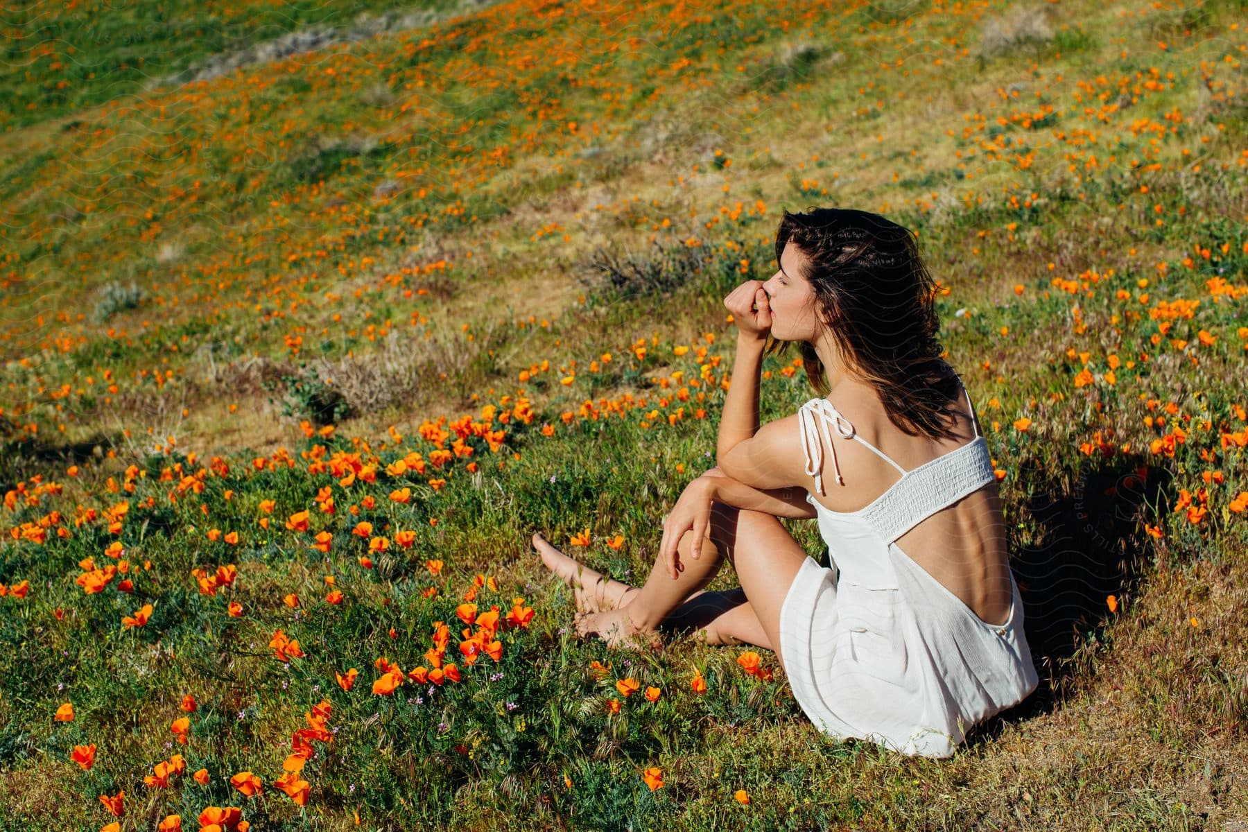 Woman sits among wildflowers on grassy slope in short summer dress.
