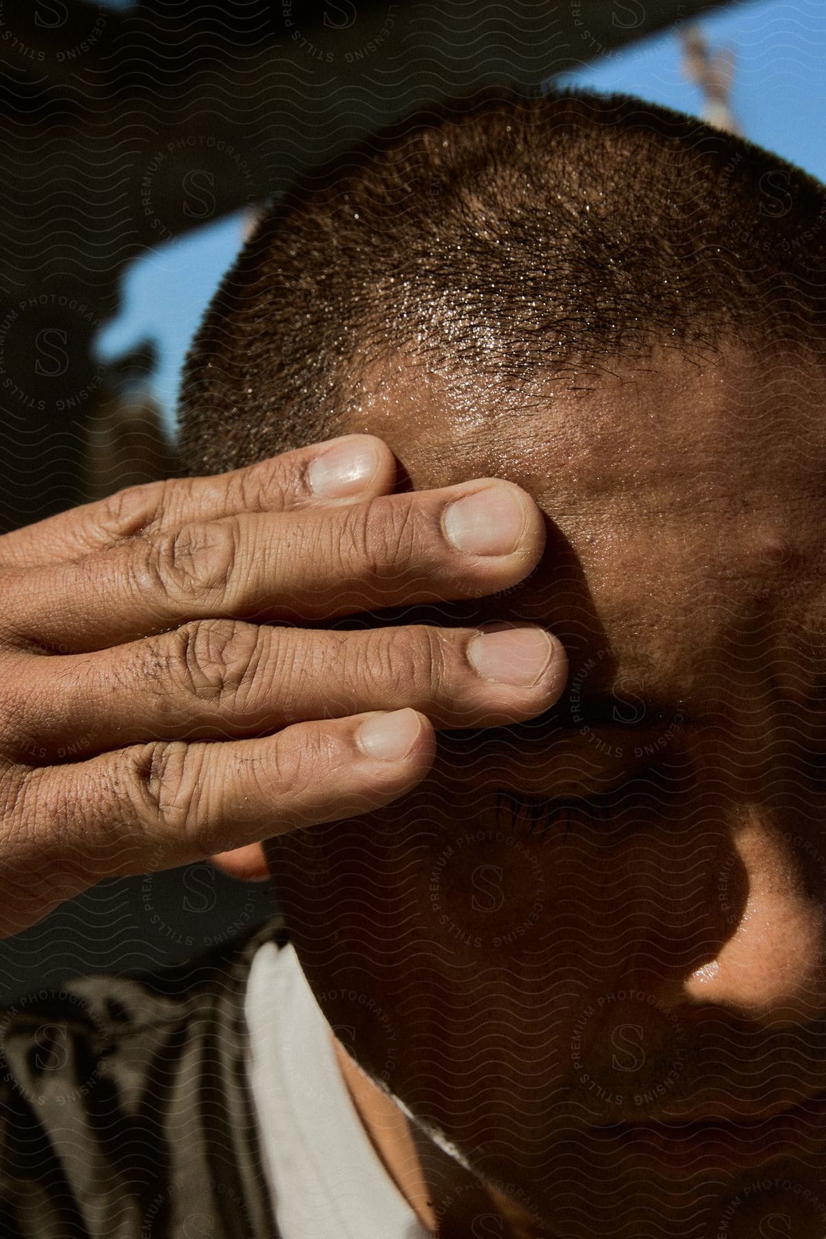 Close-up of a person holding their forehead with sunlight casting shadows on the face.