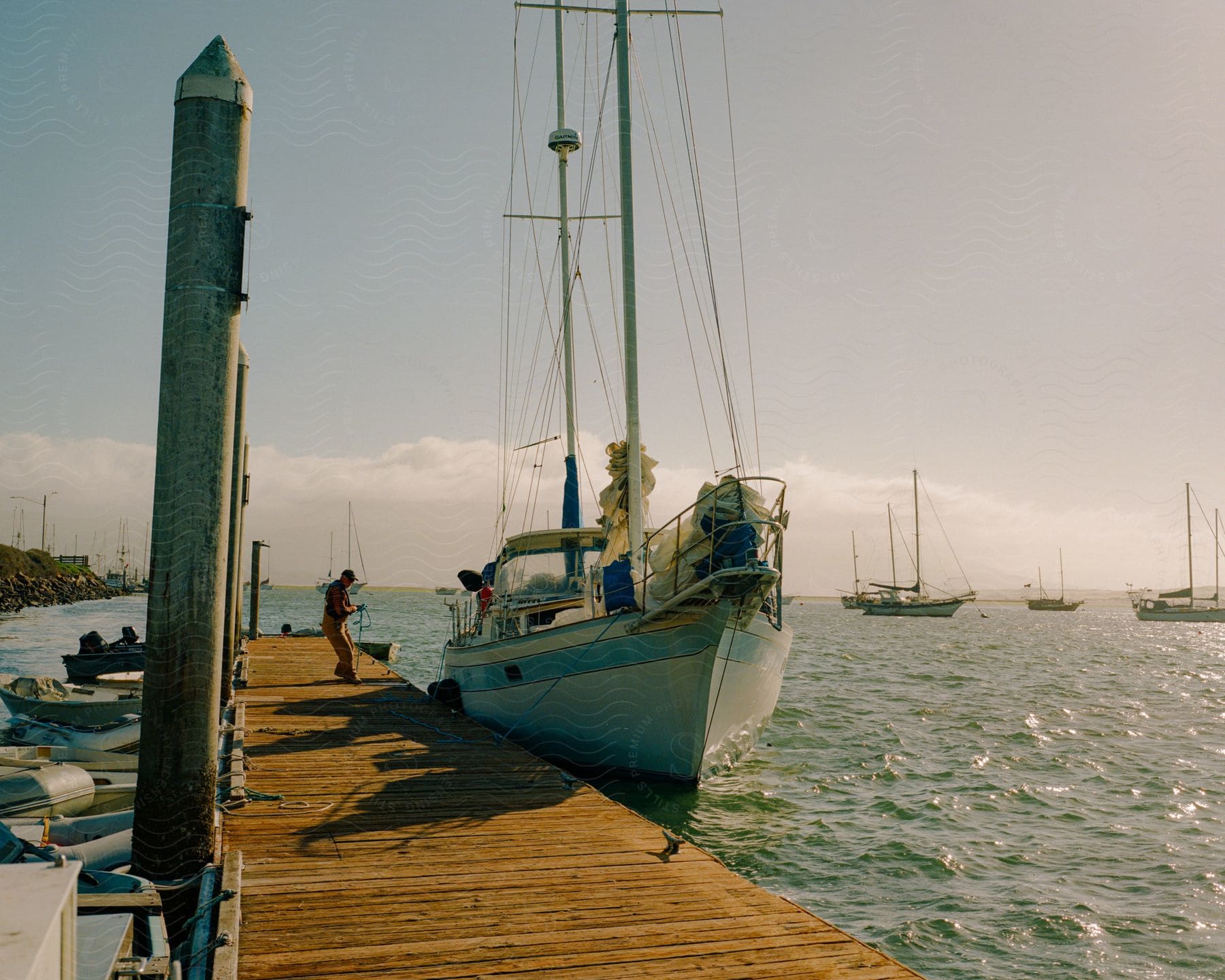 A man stands on the pier near a boat as boats sail in the water under a cloudy sky