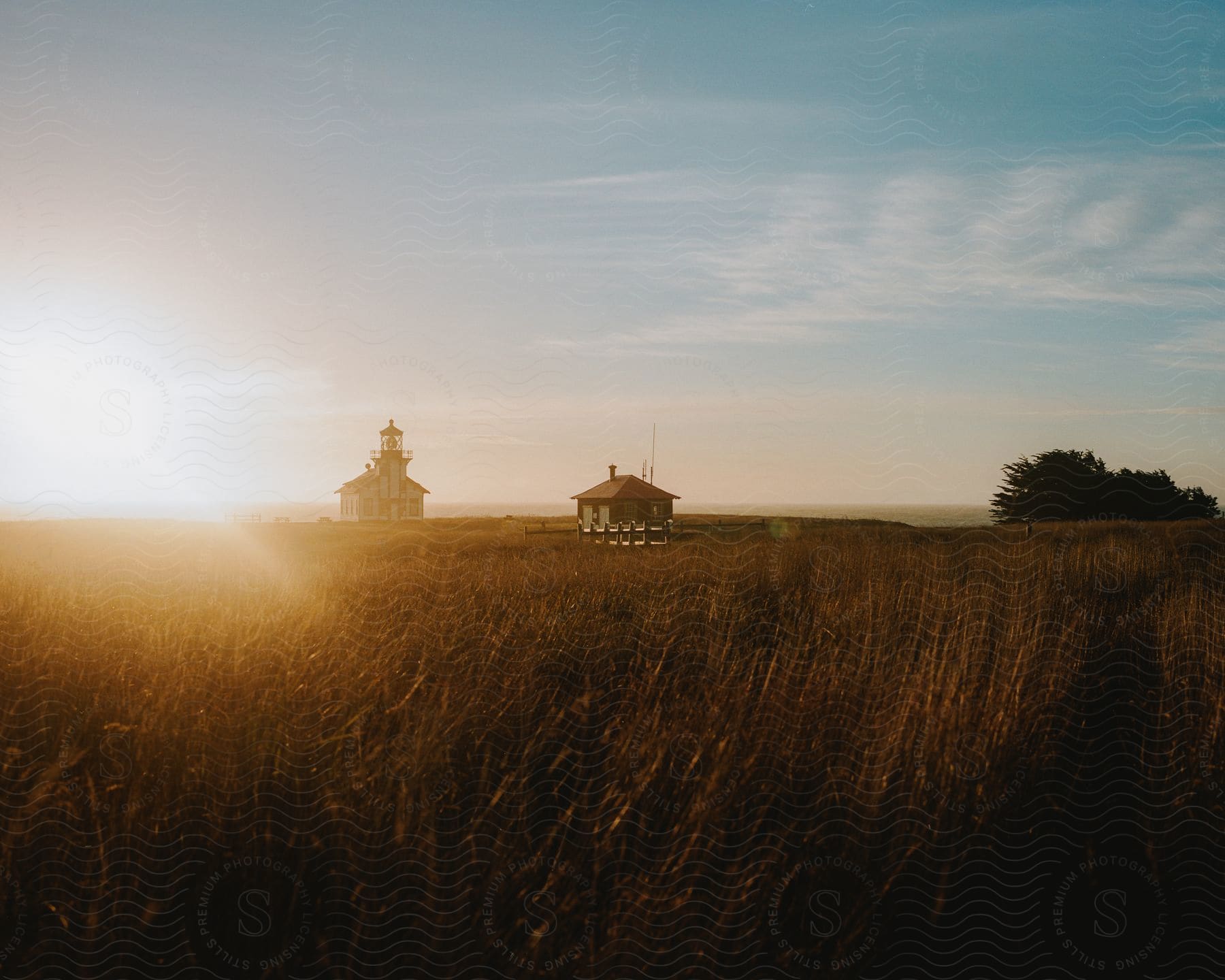 A lighthouse and a small garage sit on a flat grassland overlooking the ocean at sunrise.