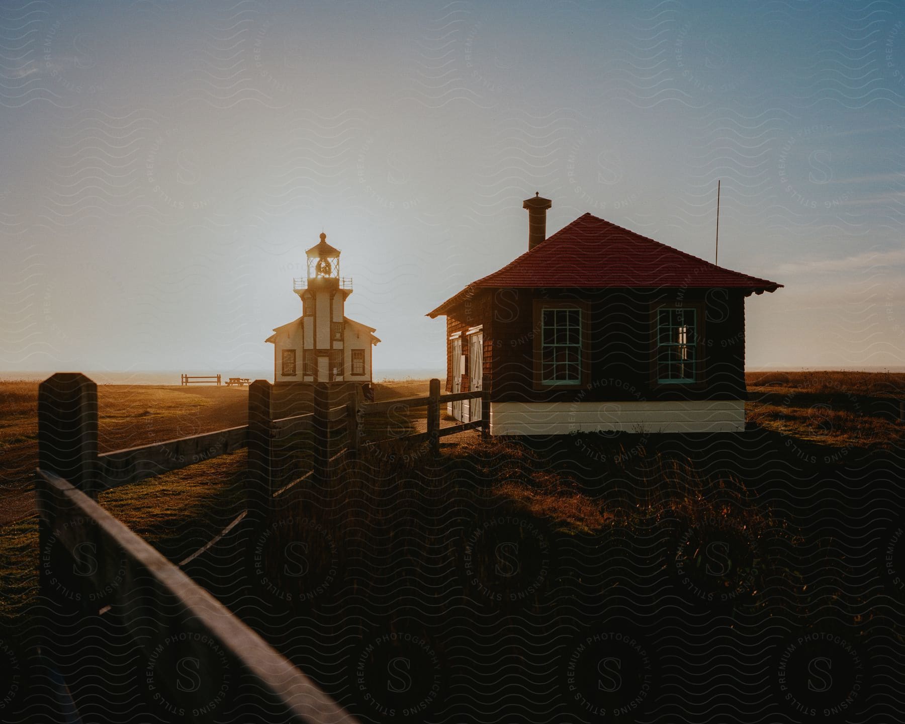 Small House In The Middle Of A Pasture And Just Behind A Church With The Morning Sun On The Horizon