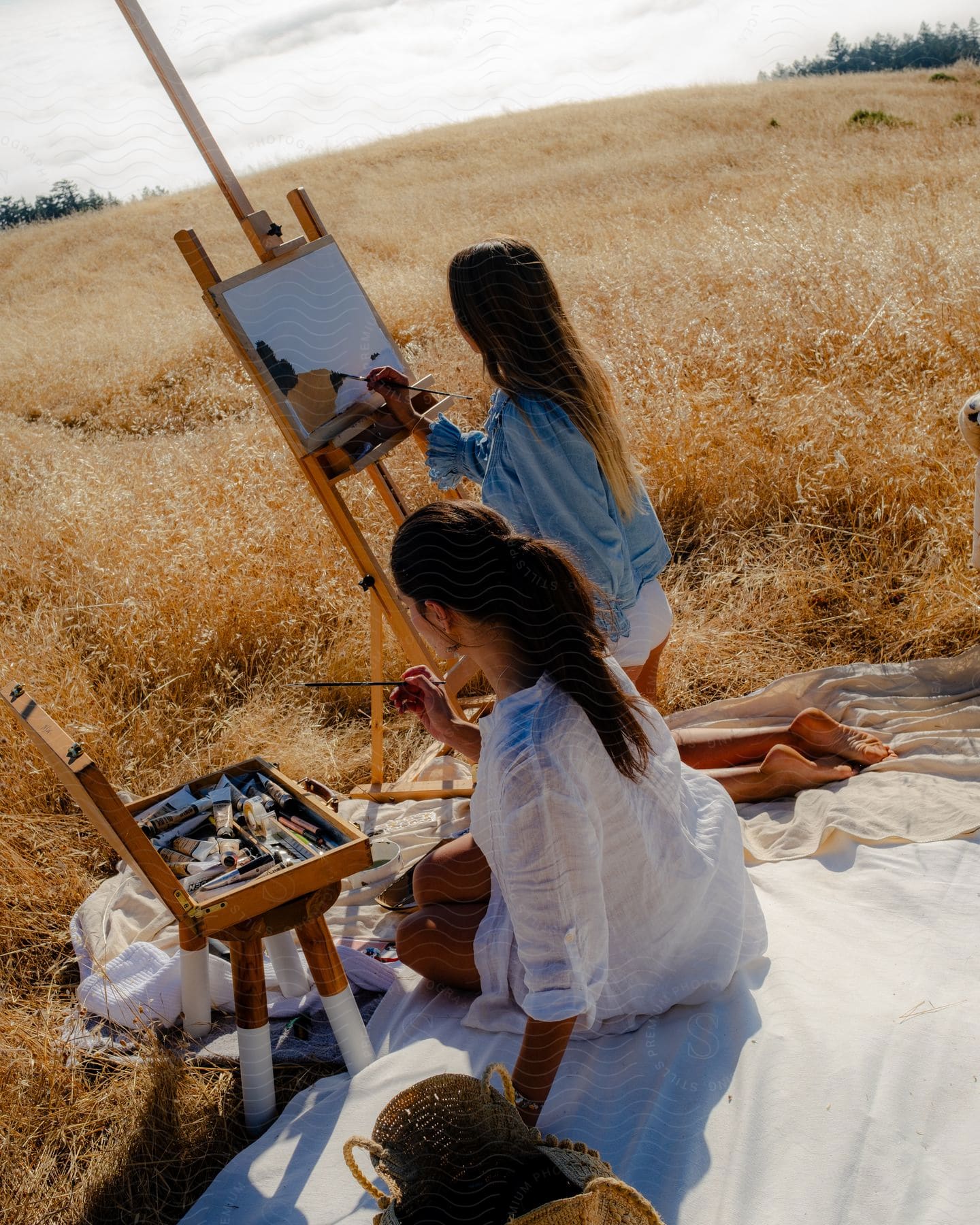 Two women are standing in a rural field painting the nature around them