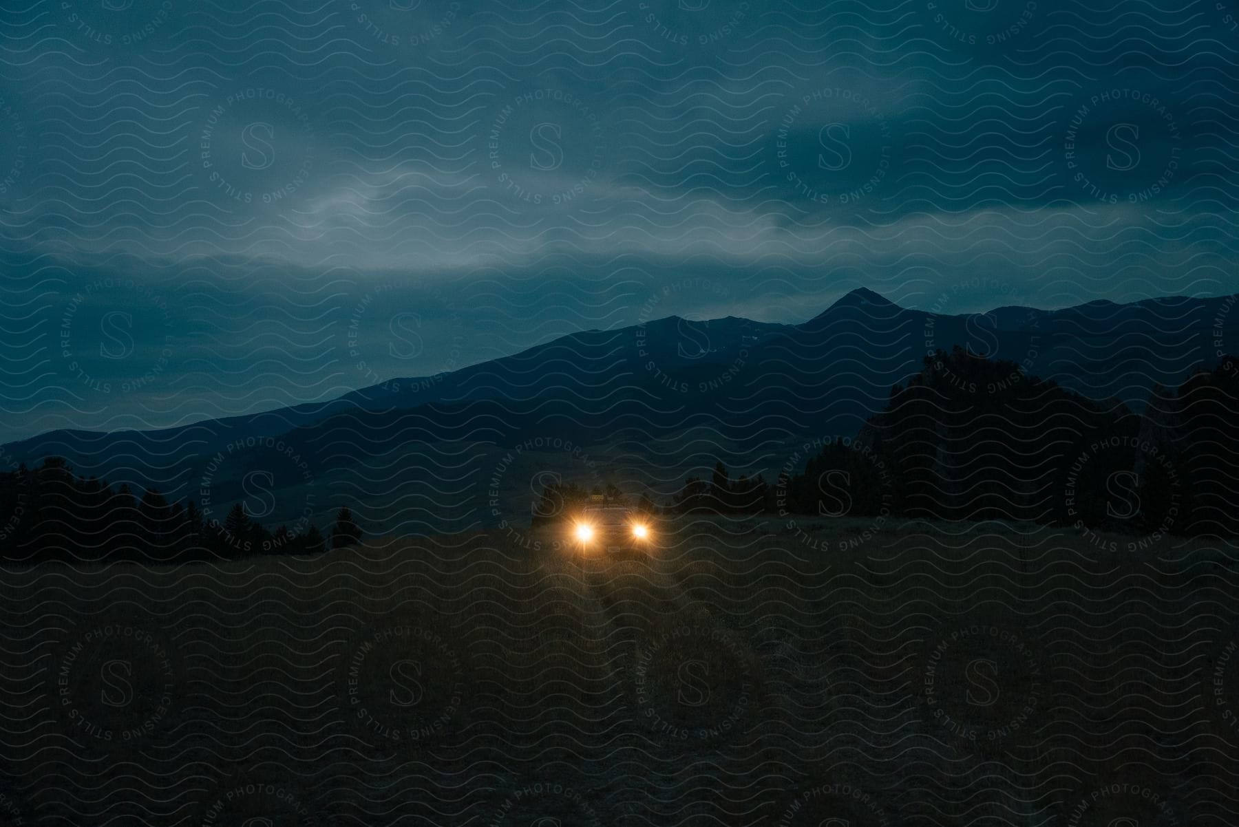 Car headlights in field with mountains in the background at dusk.