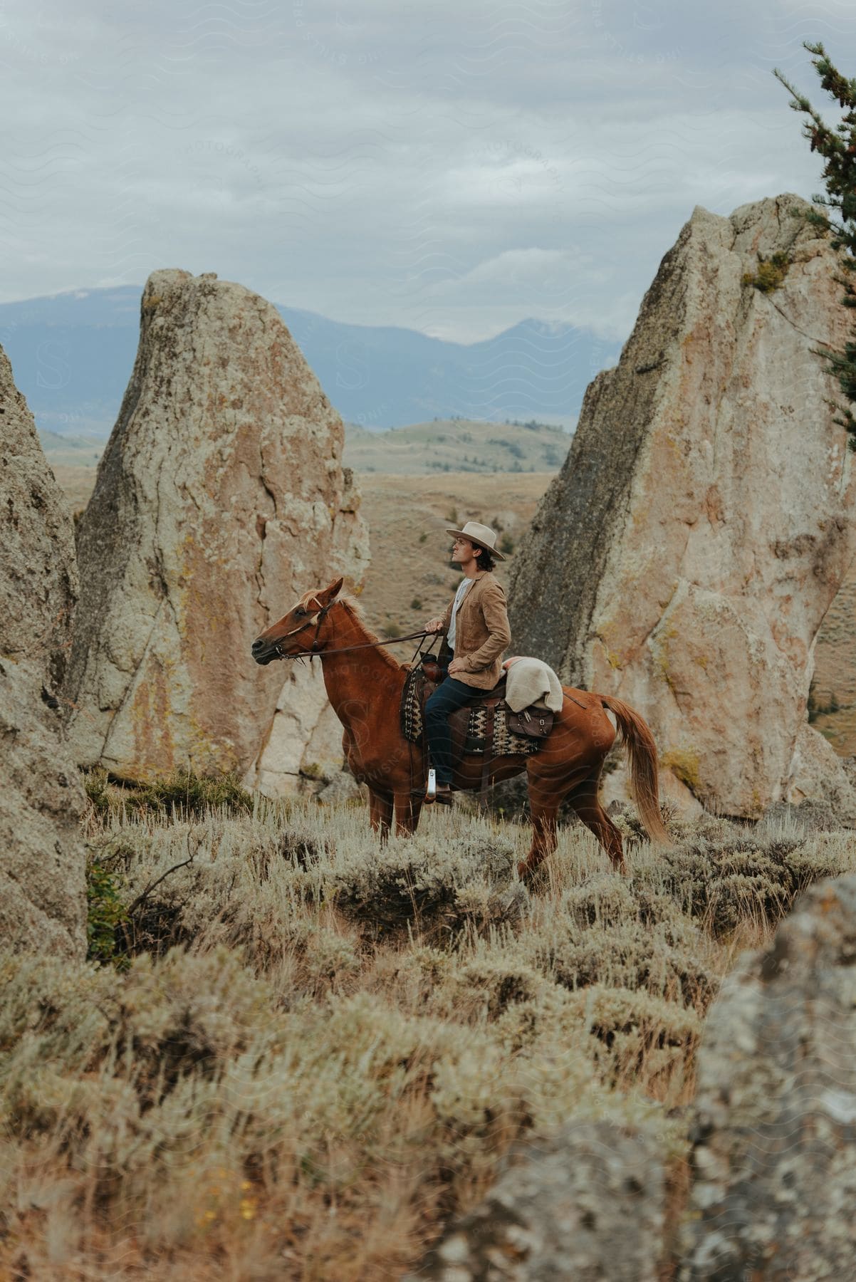 a man riding a horse while wearing a cowboy hat close to a rocky terrain