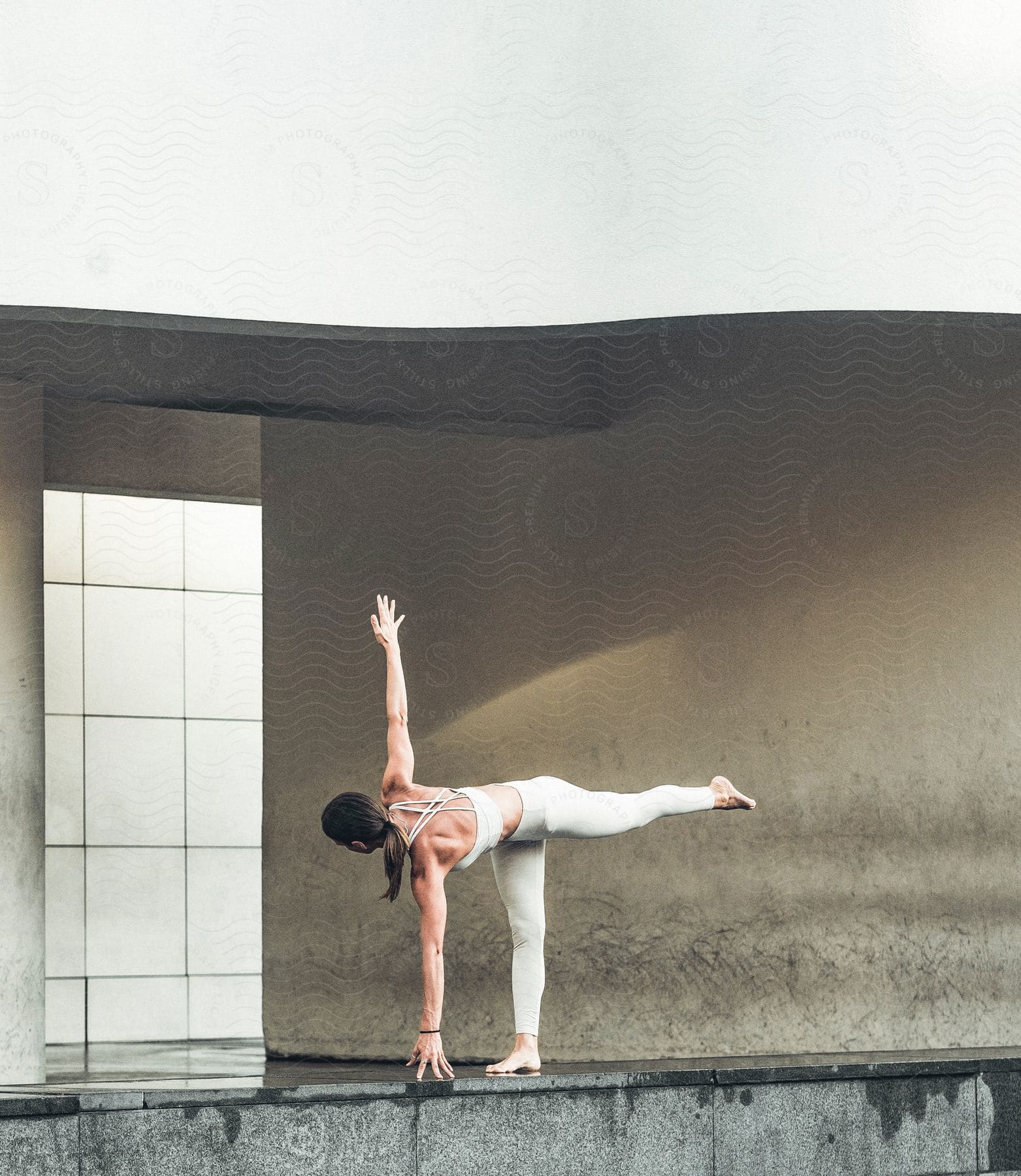 A woman is stretching with one hand on the floor and the other is up while one of her legs is on the floor and the other is pointed behind her