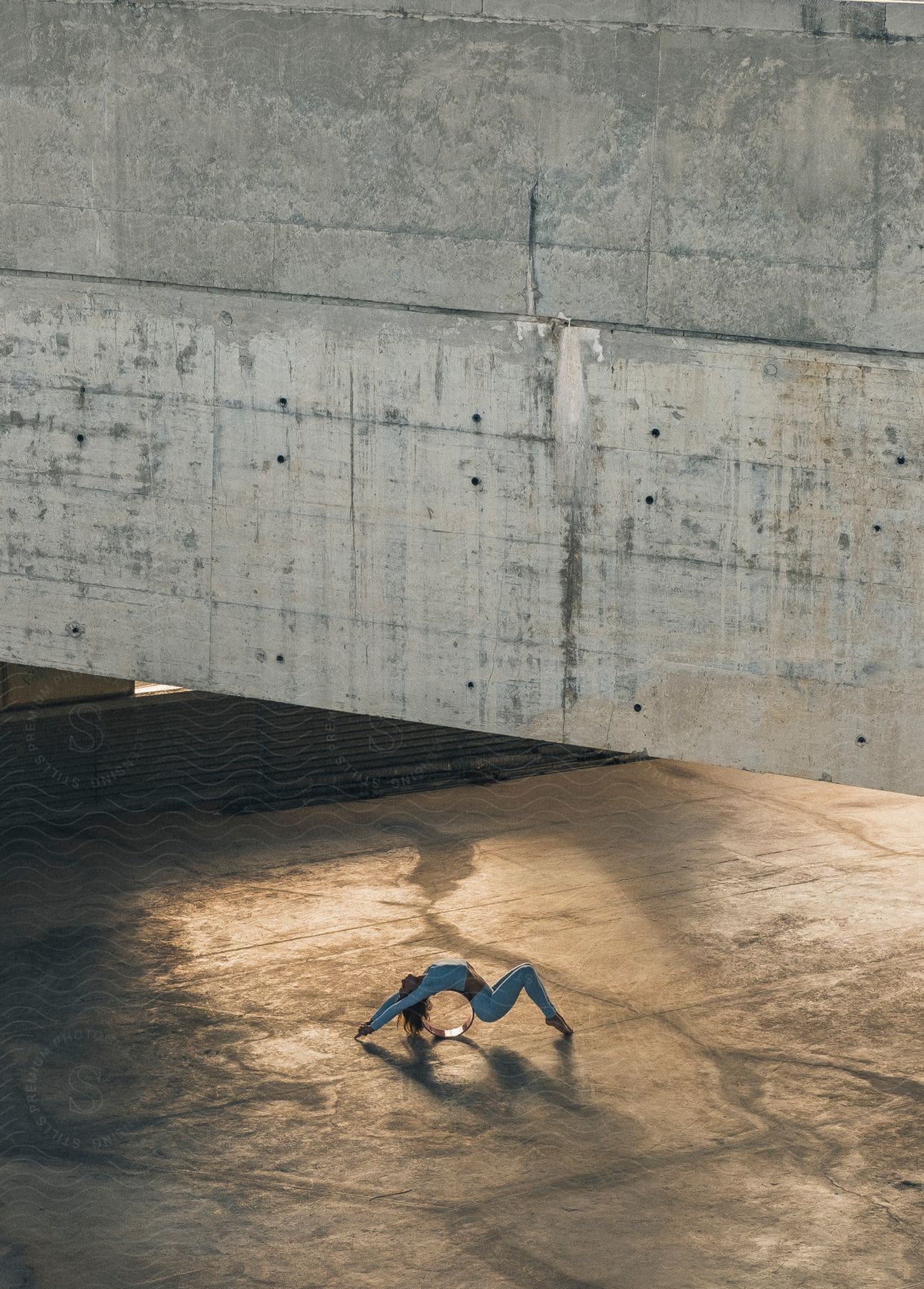 A woman is outside near a wall practicing yoga as she stretches doing a backbend