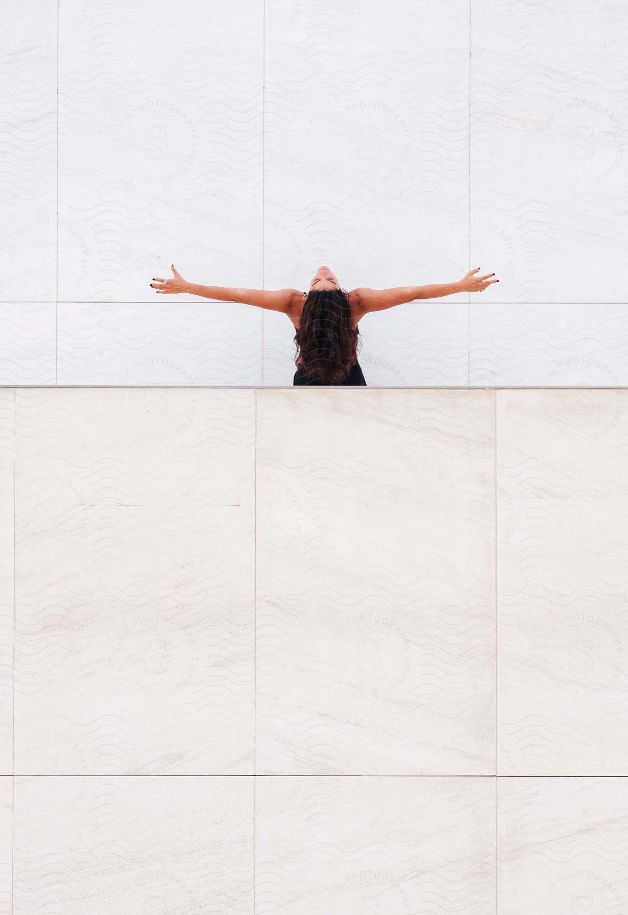 Woman with head tilted back and arms open in front of a white marble wall.