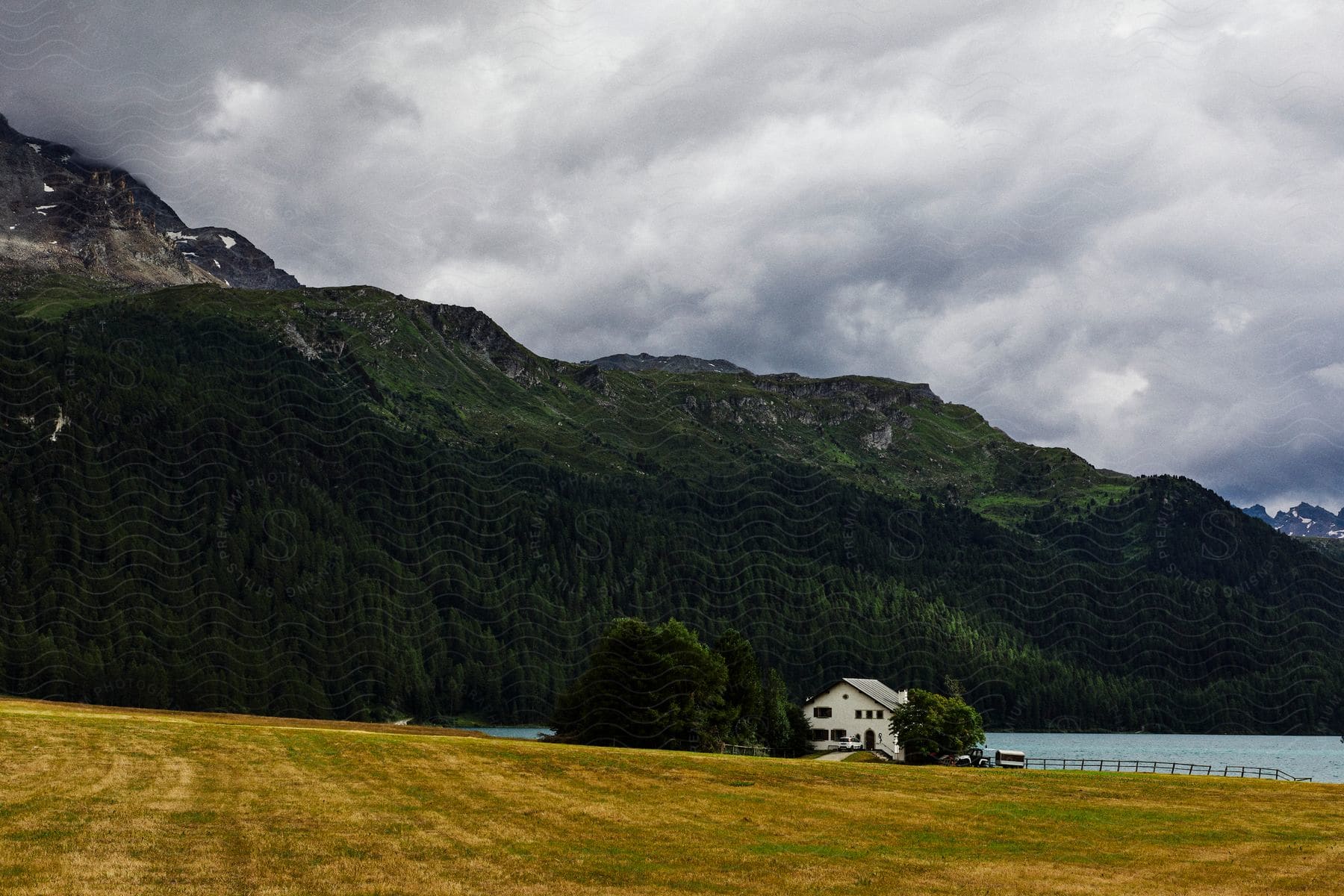 House by a lake with mountains and cloudy sky in the background.